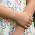 A girl's wrist wearing a silver bracelet with a flower charm, against a floral dress background.