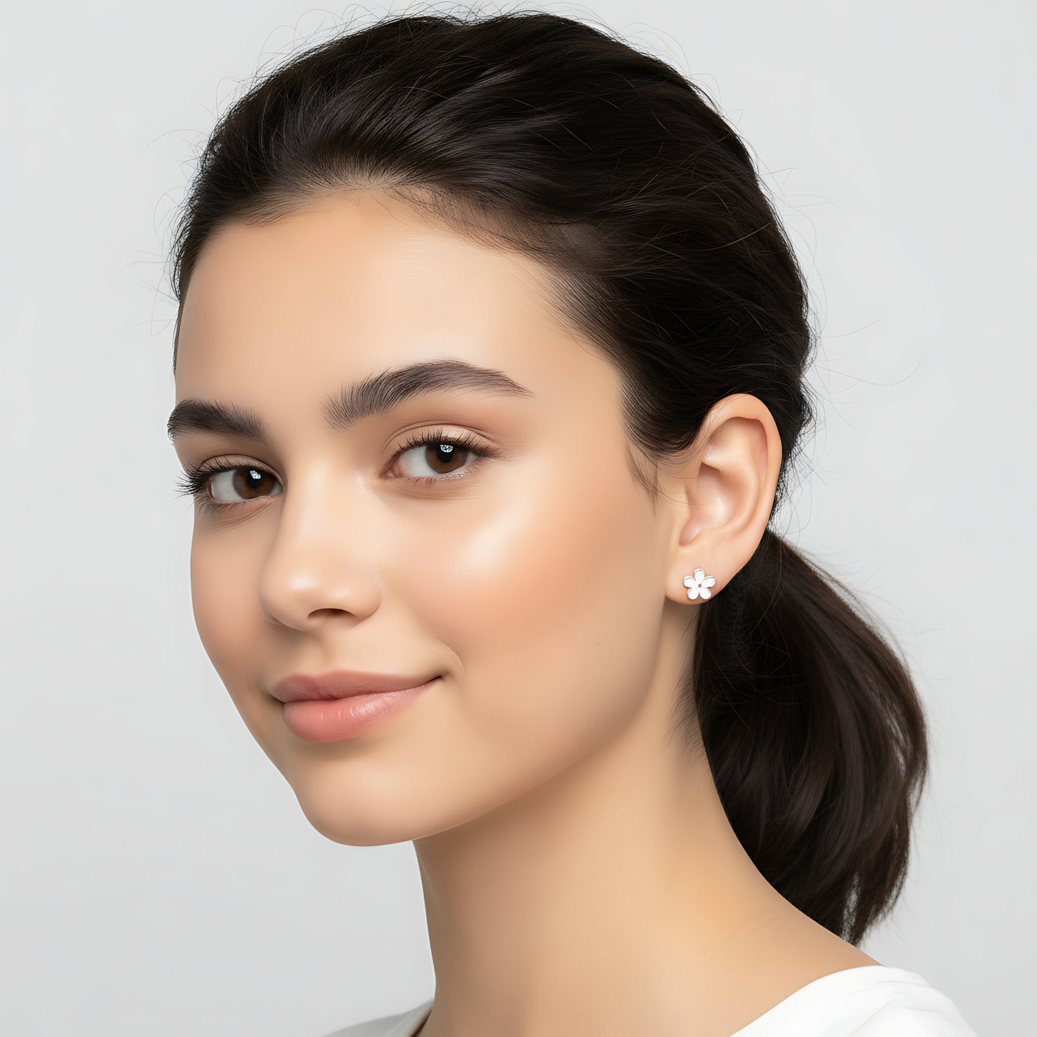 Close-up of a woman wearing a silver floral stud earring against a plain background