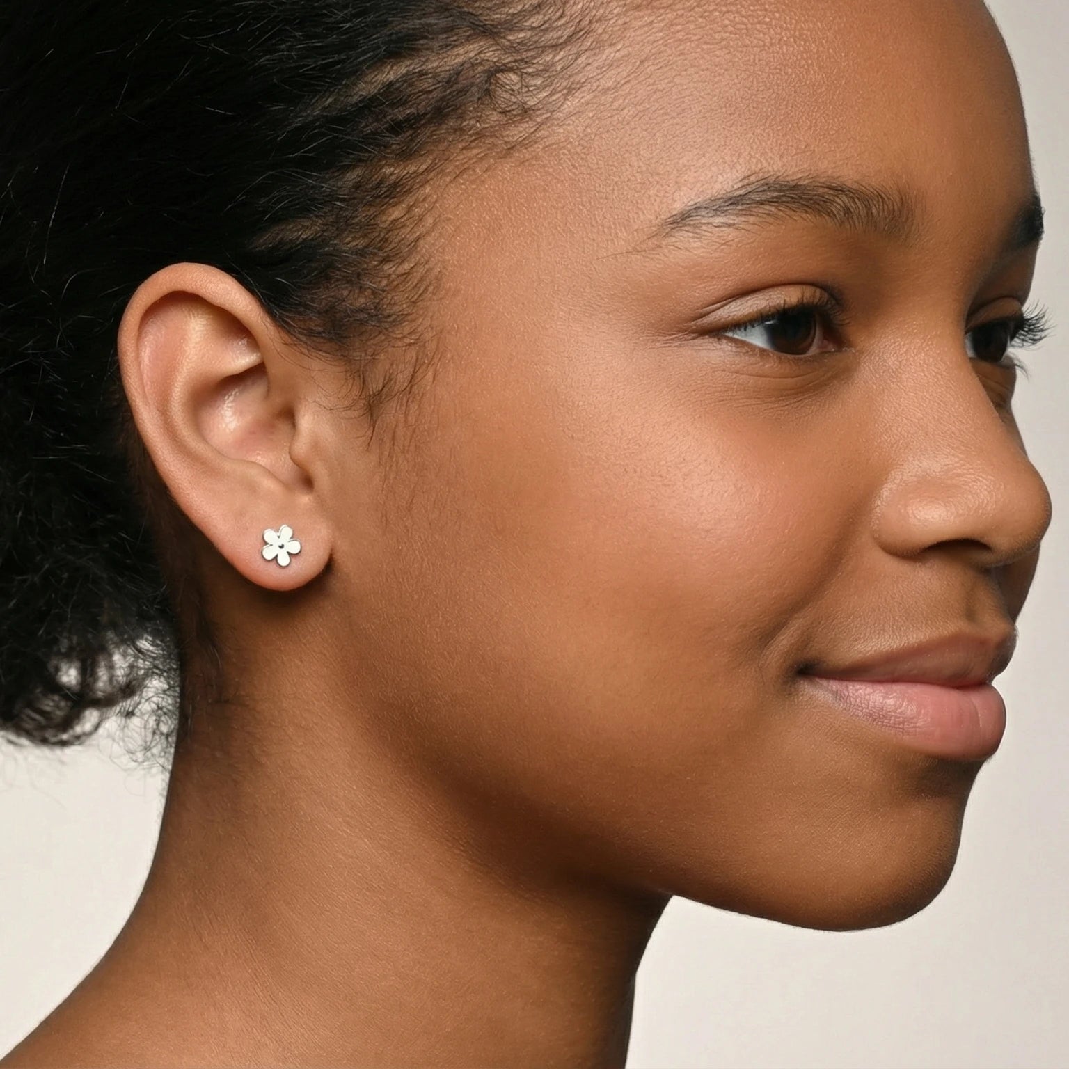 Close-up of a girl wearing a silver floral stud earring against a plain background