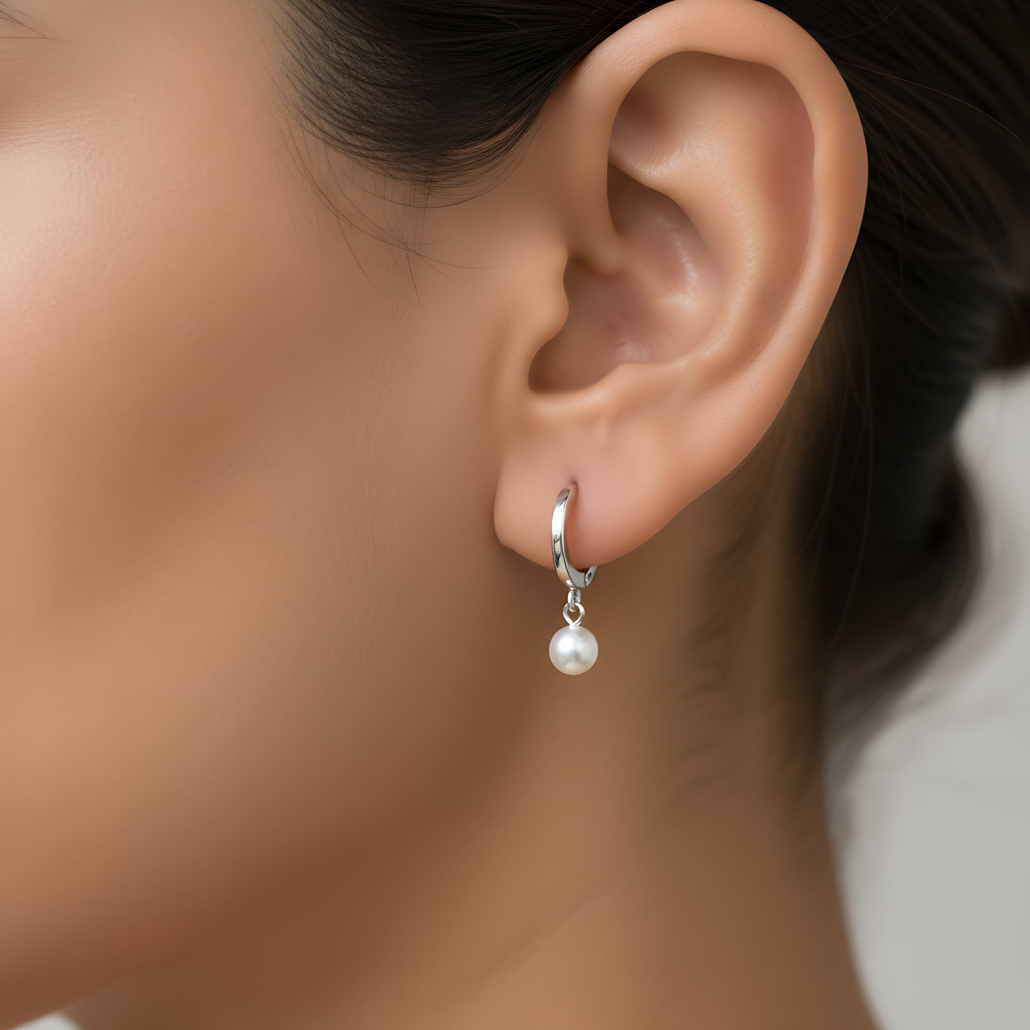 Close-up of an ear wearing a silver hoop earring with a fresh water pearl charm 