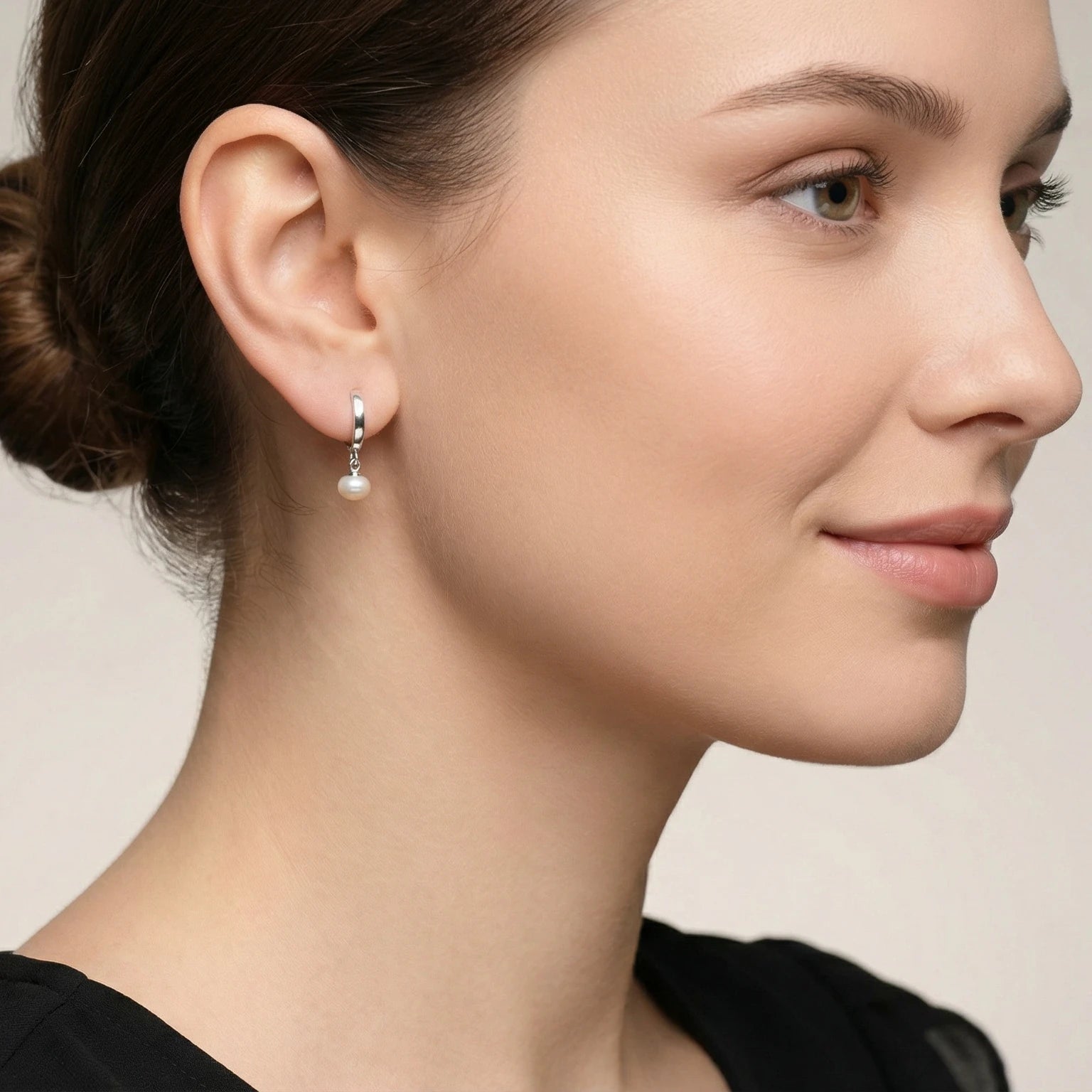 Close-up of a female wearing a silver hoop earring with a fresh water pearl charm and a black dress