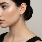 Close-up of an ear wearing a geometric silver hoop earring with a plain background