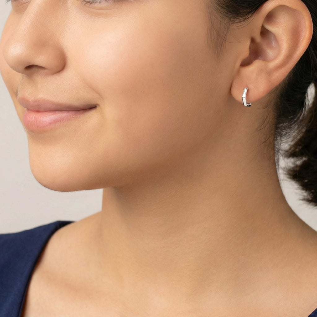 Woman with styled hair and silver geometric half hoop stud earrings against a blurred background