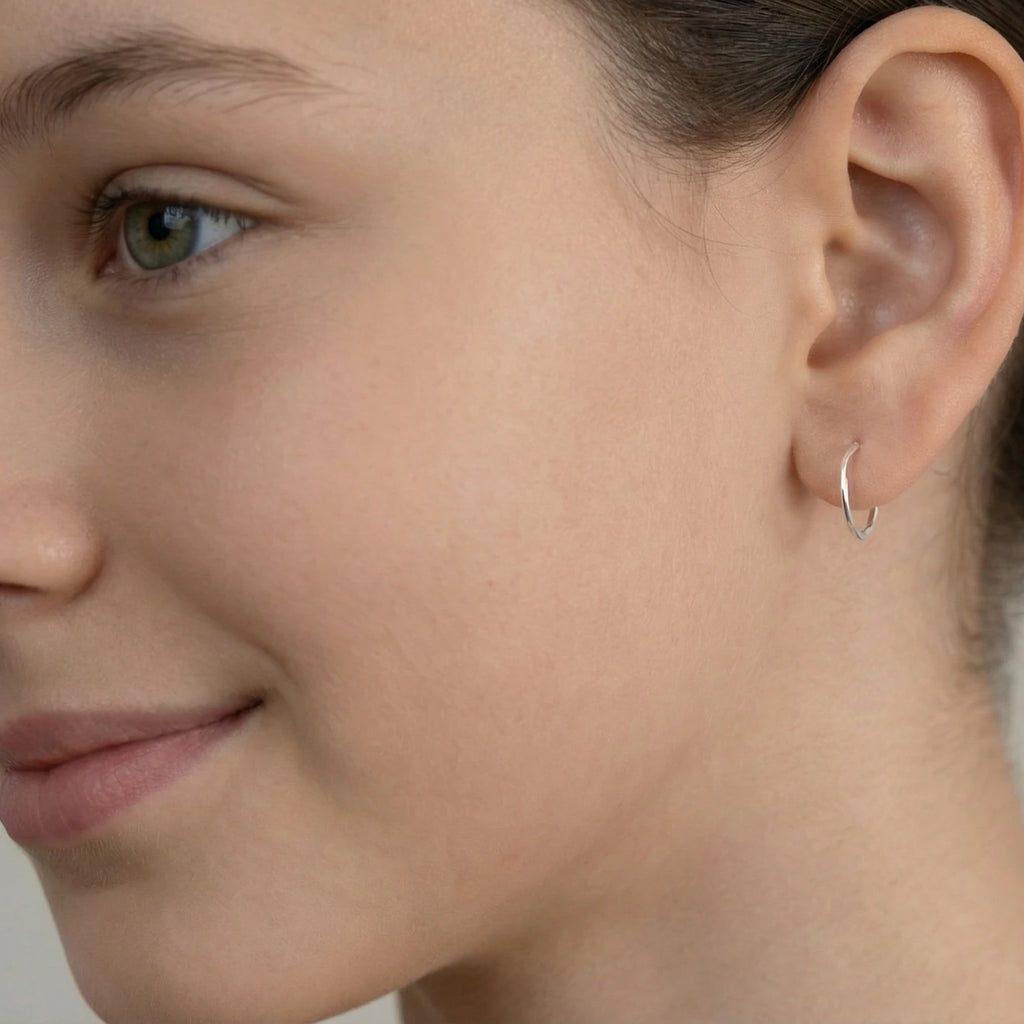 Closeup of a girl wearing a silver half hoop stud earring on a plain background
