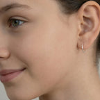 Closeup of a girl wearing a silver half hoop stud earring on a plain background