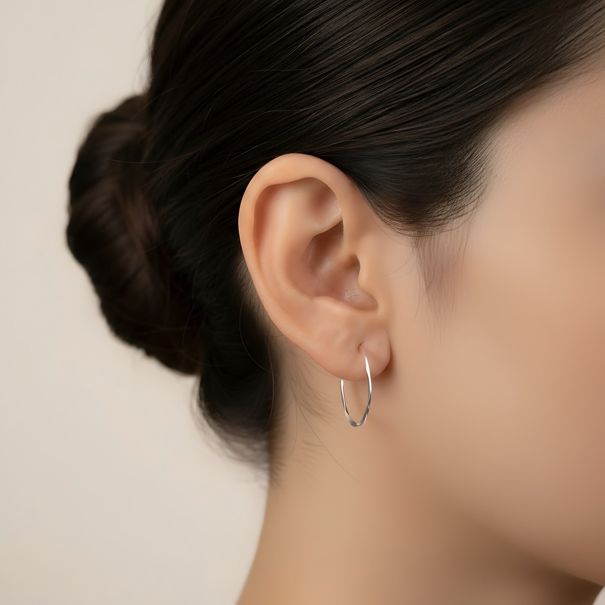 Close-up of an ear wearing a silver hammered half hoop stud earring with a neutral background