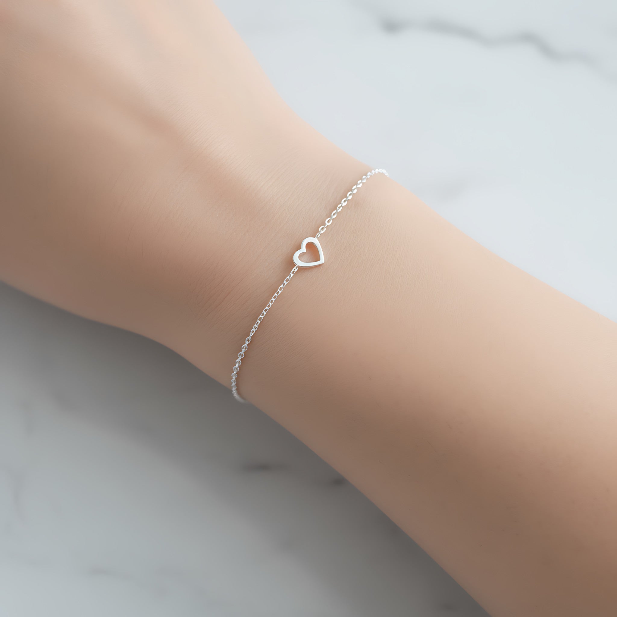 Silver bracelet with a heart charm on a wrist against a light background