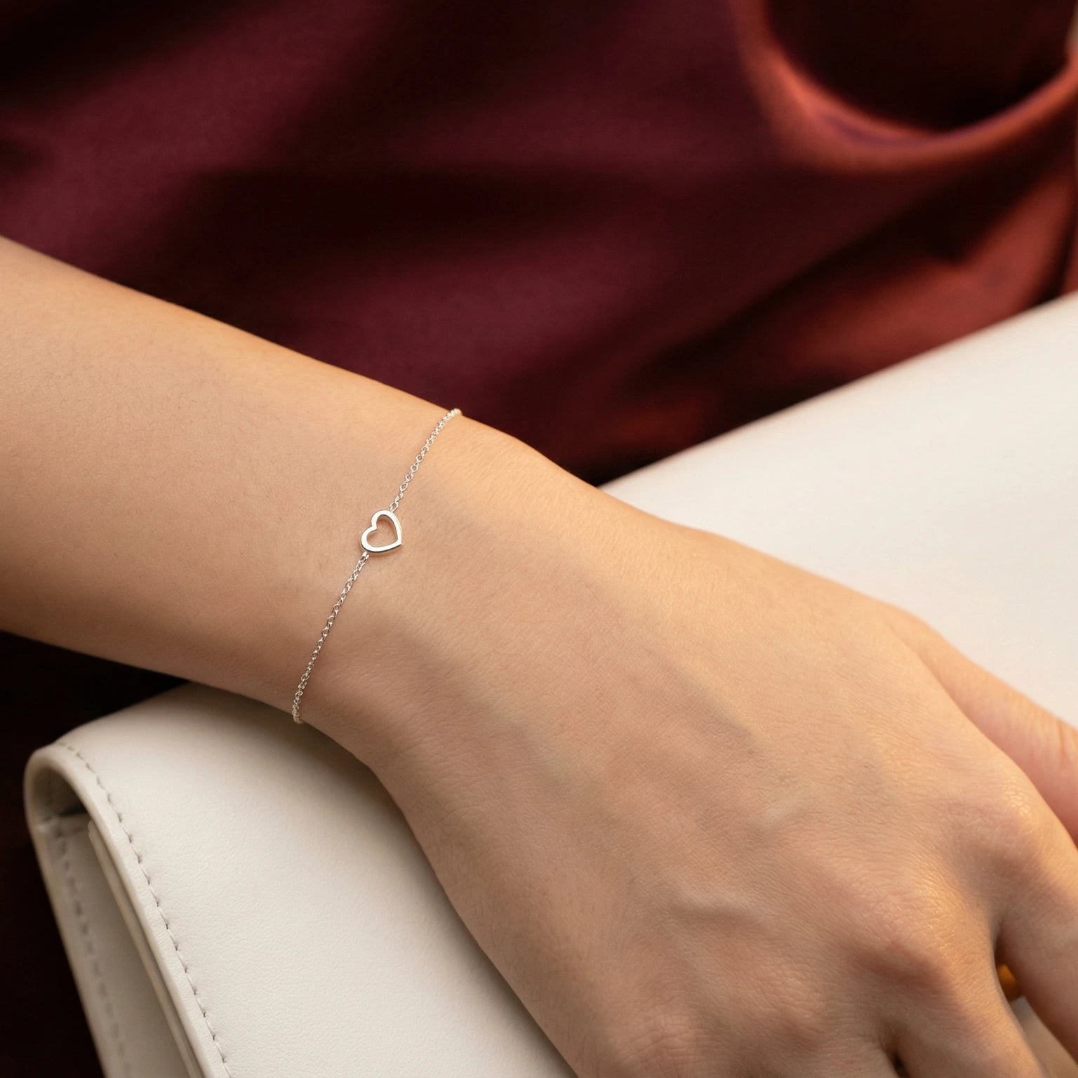 Female wearing a Silver bracelet with a heart charm on a wrist and a red dress with a white clutch in her hand