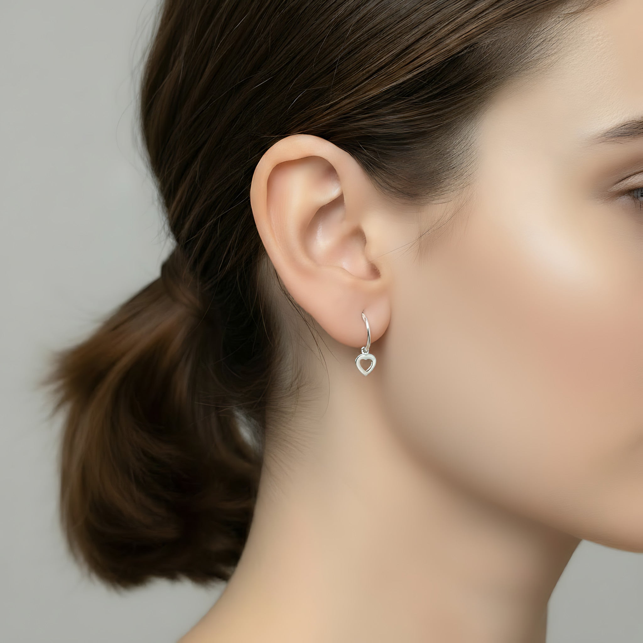 Close-up of a woman wearing a heart-shaped charm hoop earring with a blurred background