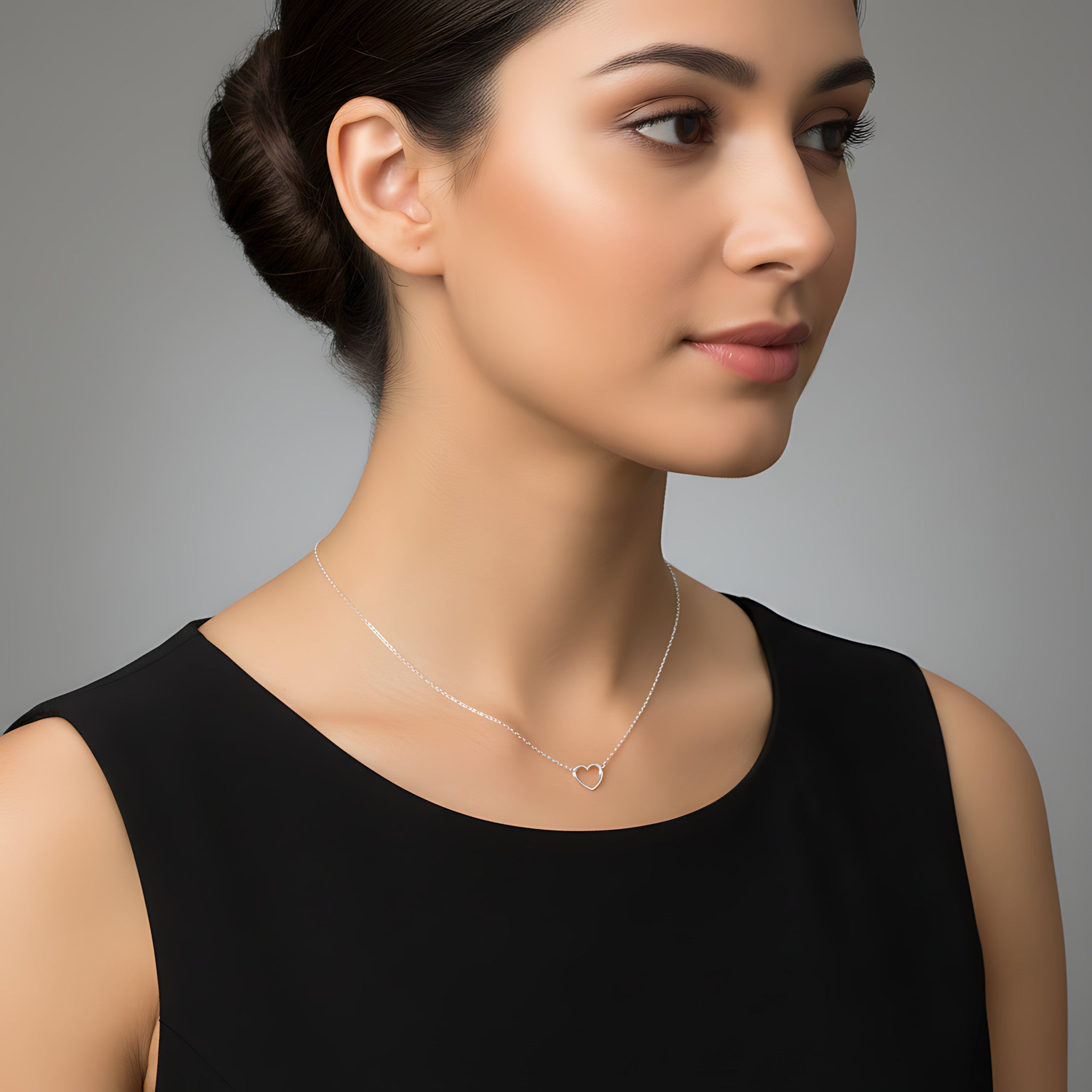 Closeup of a female wearing a silver necklace with a small hart pendant against a neutral background