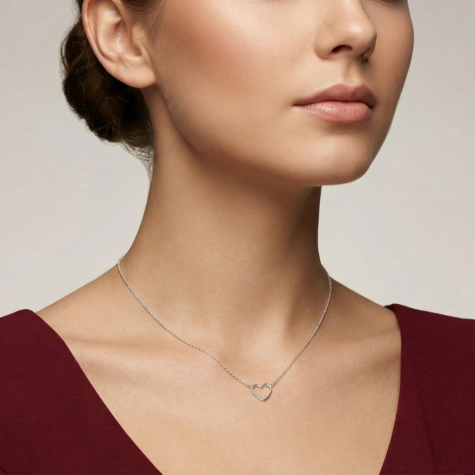 Closeup of a female wearing a silver necklace with a small hart pendant against a neutral background