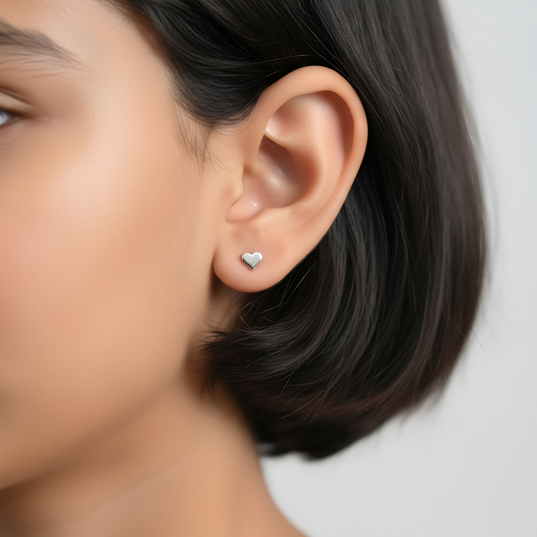Closeup of a girl wearing a silver heart shape stud earring on a plain background