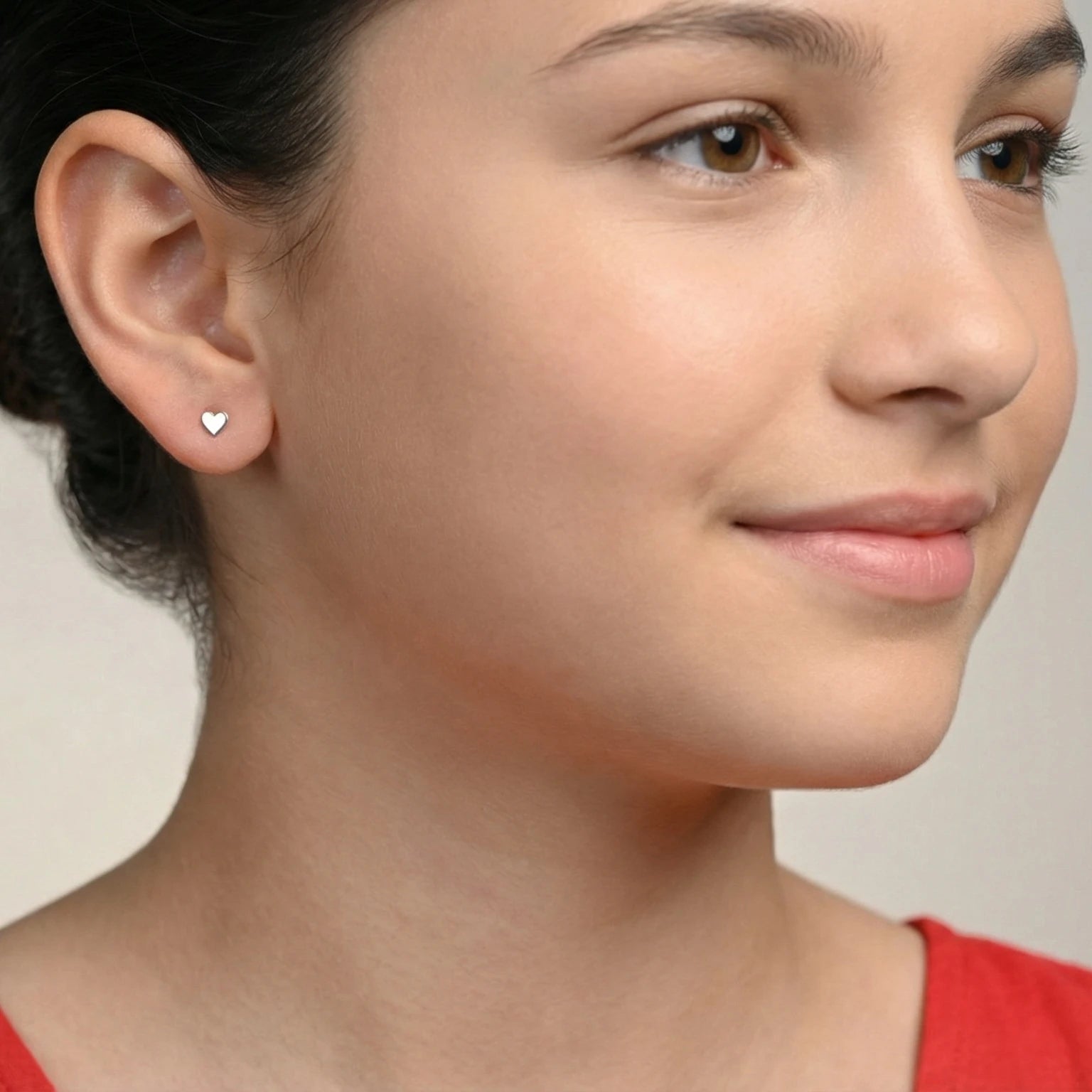 Closeup of a girl wearing a silver heart shape stud earring on a plain background