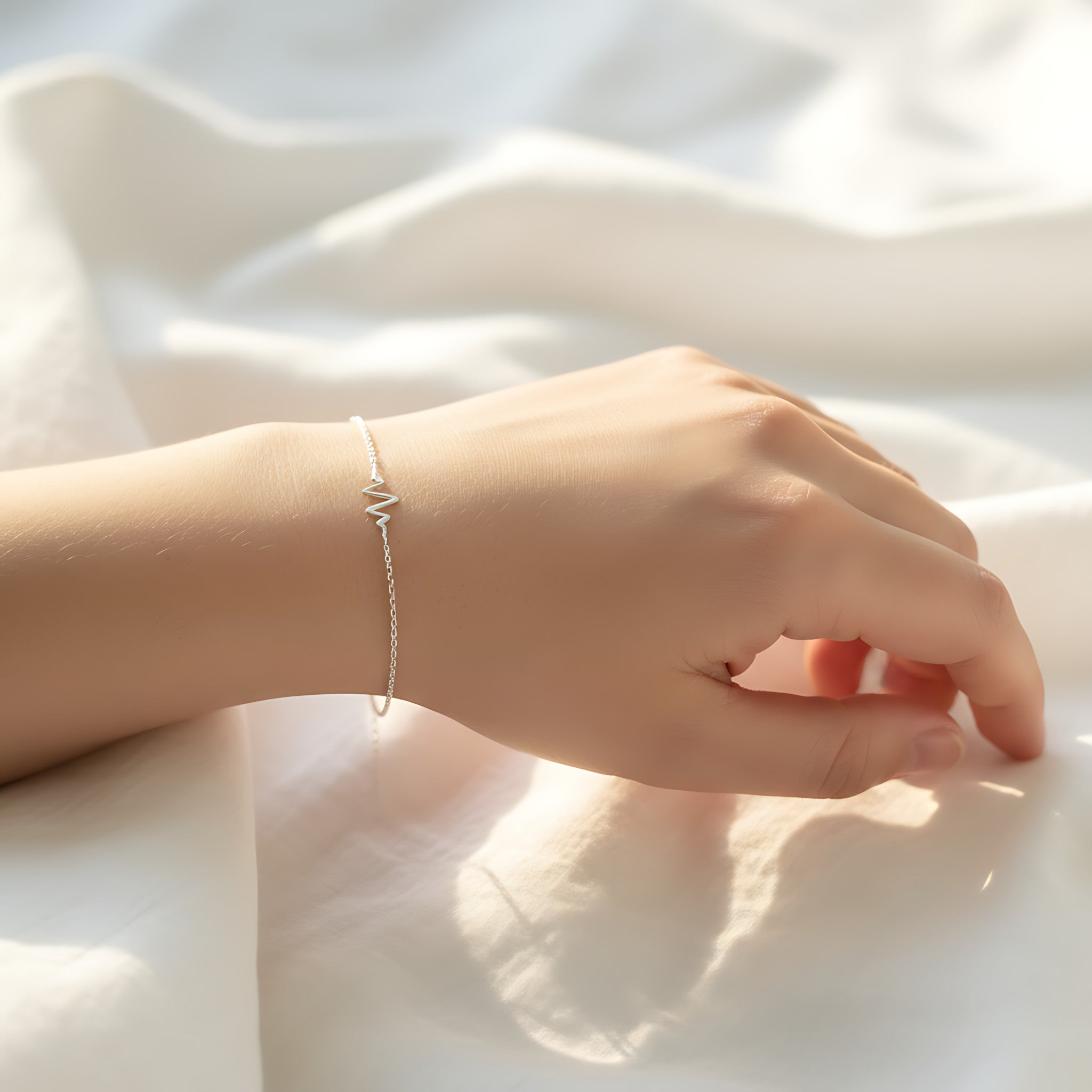 Hand wearing a silver hearbeat bracelet on a light fabric background