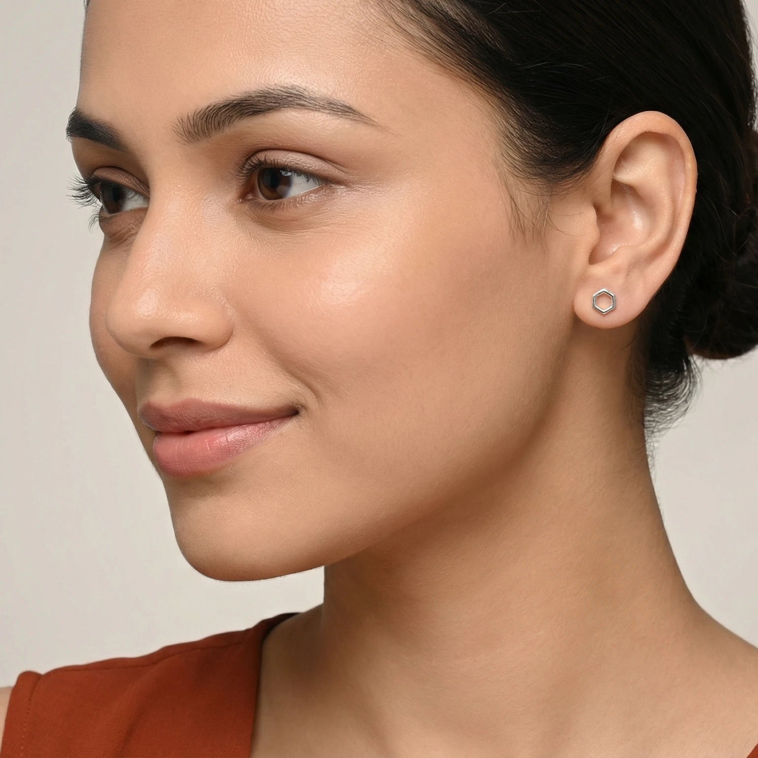 Closeup of a woman wearing a rust colour dress and a hexagon shaped silver stud earring