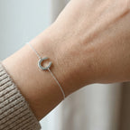 Silver bracelet with a horseshoe charm on a wrist against a neutral background