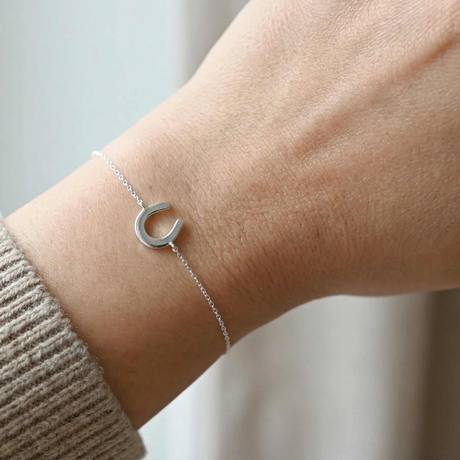 Silver bracelet with a horseshoe charm on a wrist against a neutral background