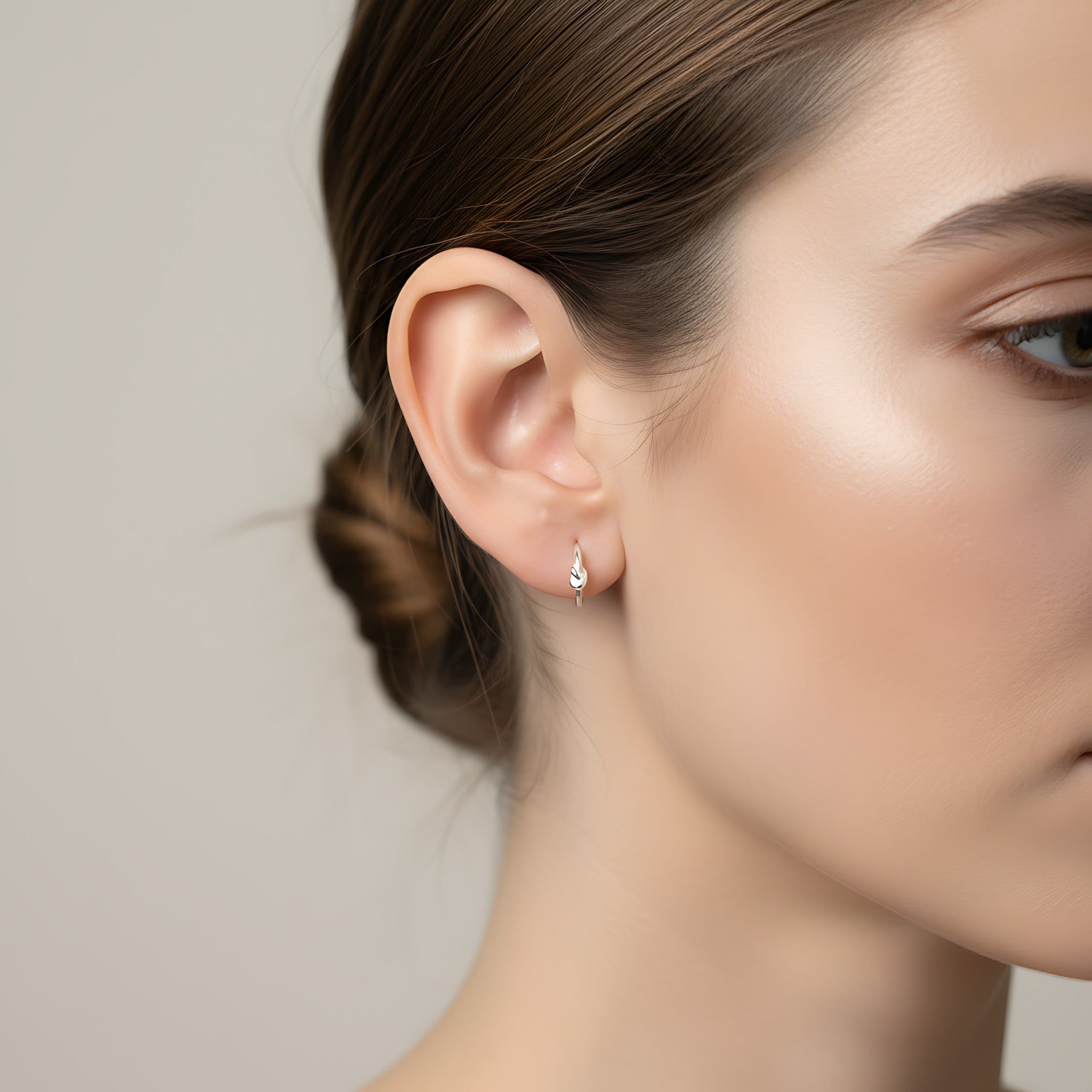 Close-up of a woman wearing a silver knot half hoop stud earring with a neutral background