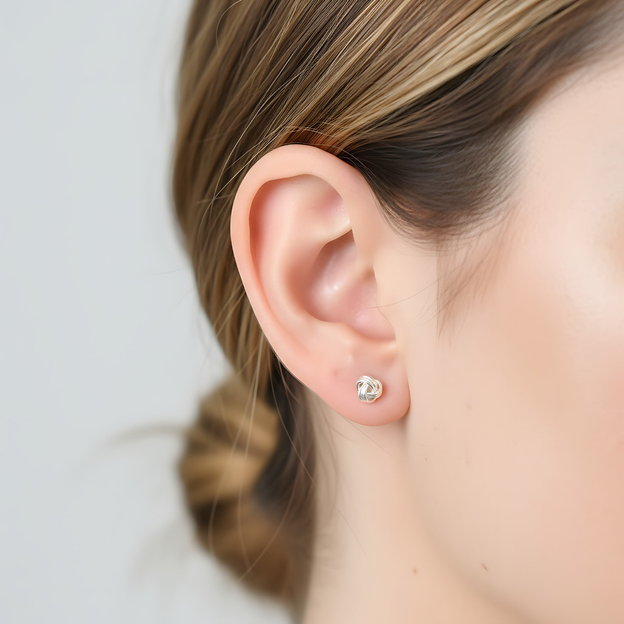 Close-up of an ear wearing a small silver knot stud earring with a blurred background