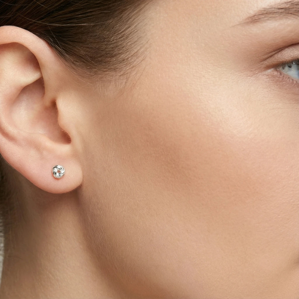 Close-up of an ear wearing a small silver knot stud earring