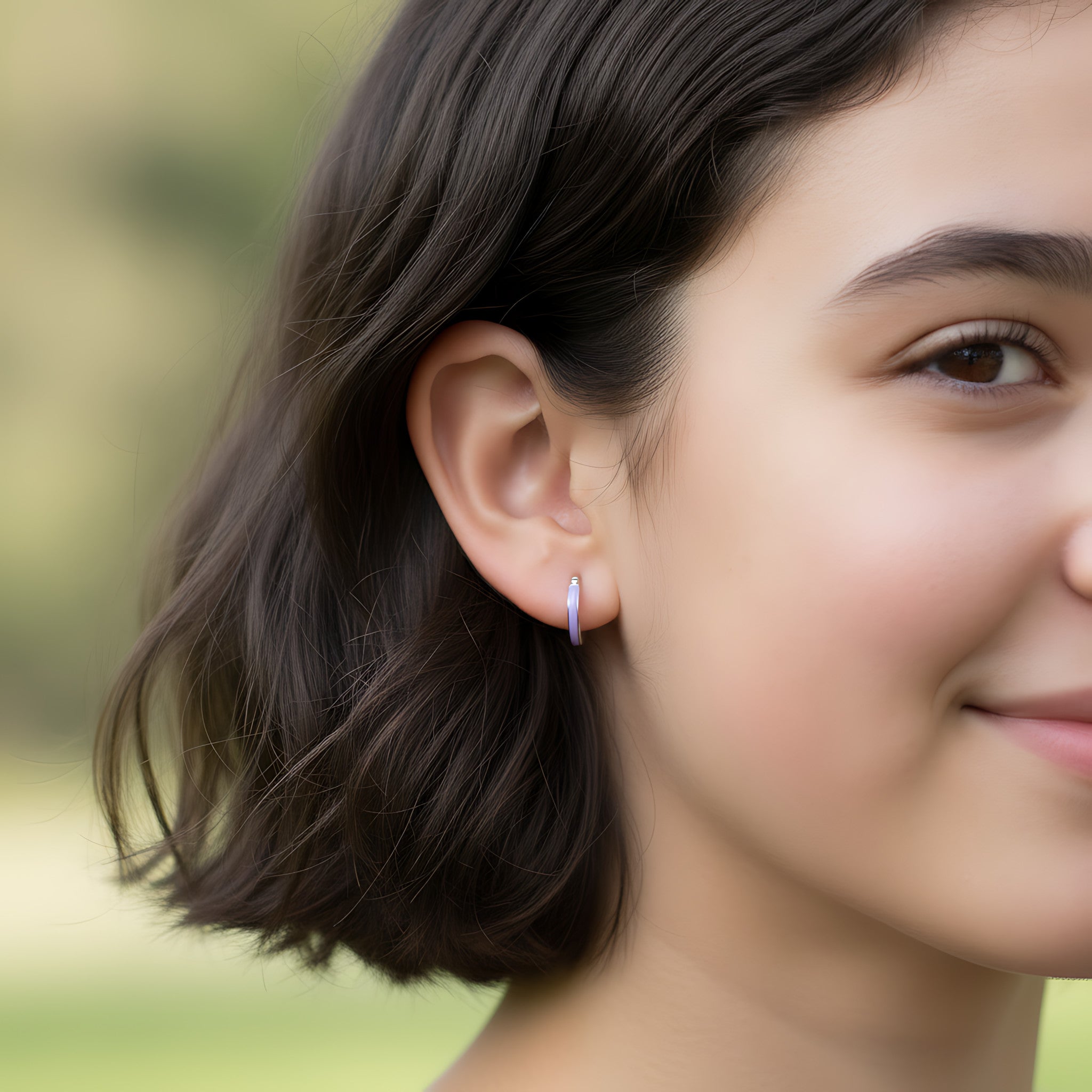 Close-up of a girl wearing a silver hoop earring having a lavender colour accent with a blurred green background