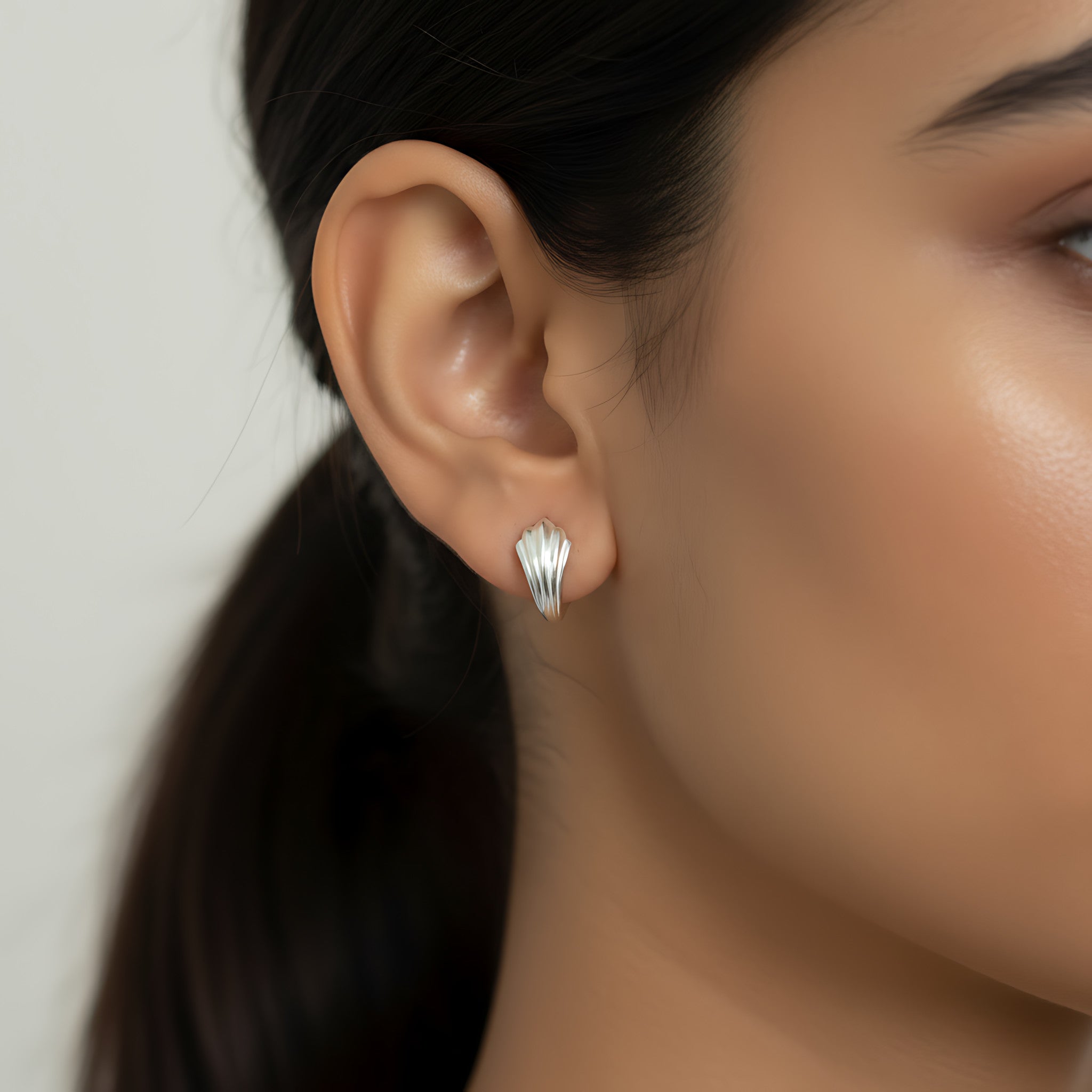 Close-up of a woman's ear wearing a small leaf silver hoop earring with a blurred background