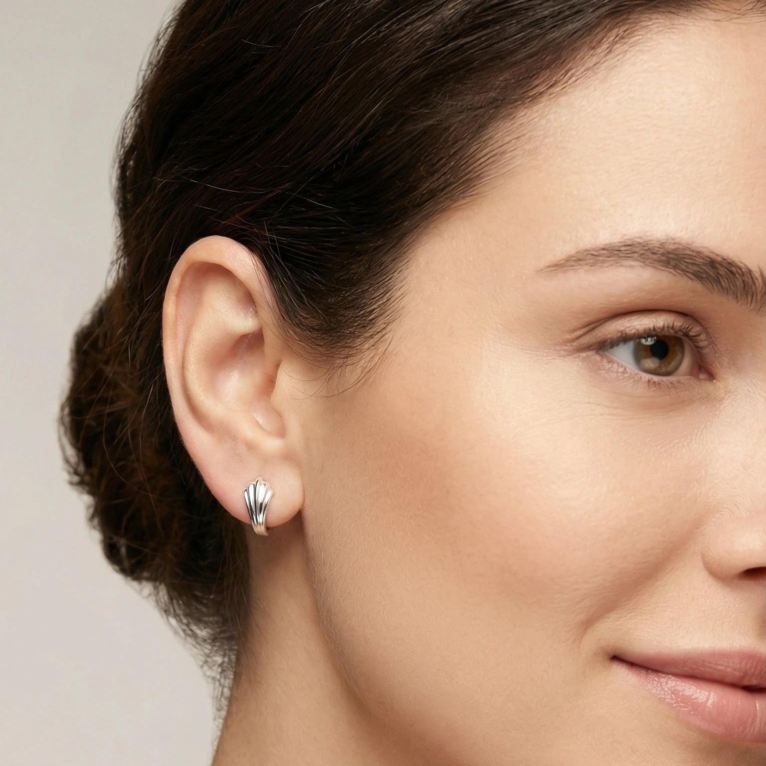 Close-up of a woman wearing a Silver Leaf Huggie Hoop Earring with a neutral background