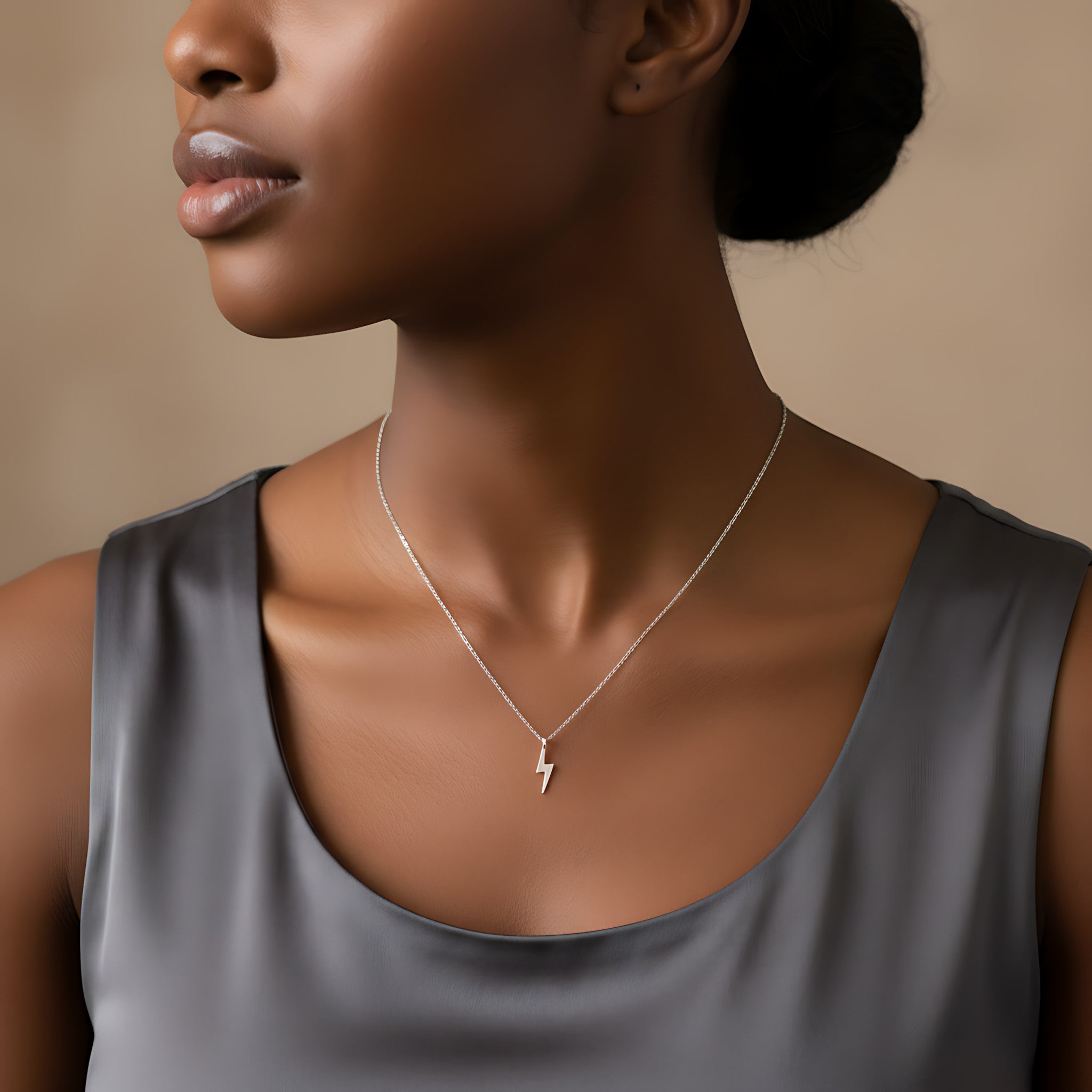 Closeup of a female wearing a silver necklace with a small lightning bolt pendant against a neutral background