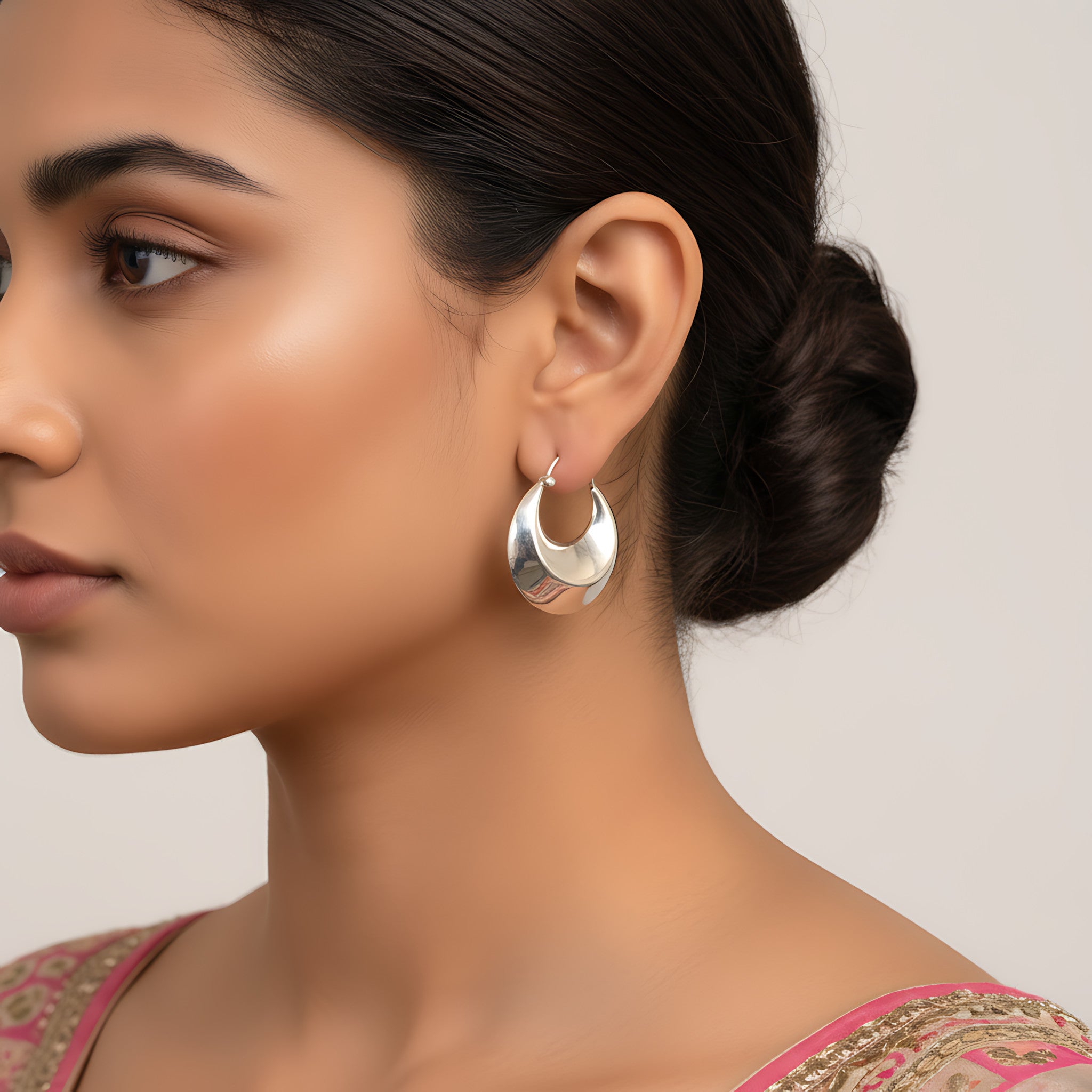 Close-up of a woman wearing shiny silver hoop earrings with a neutral background