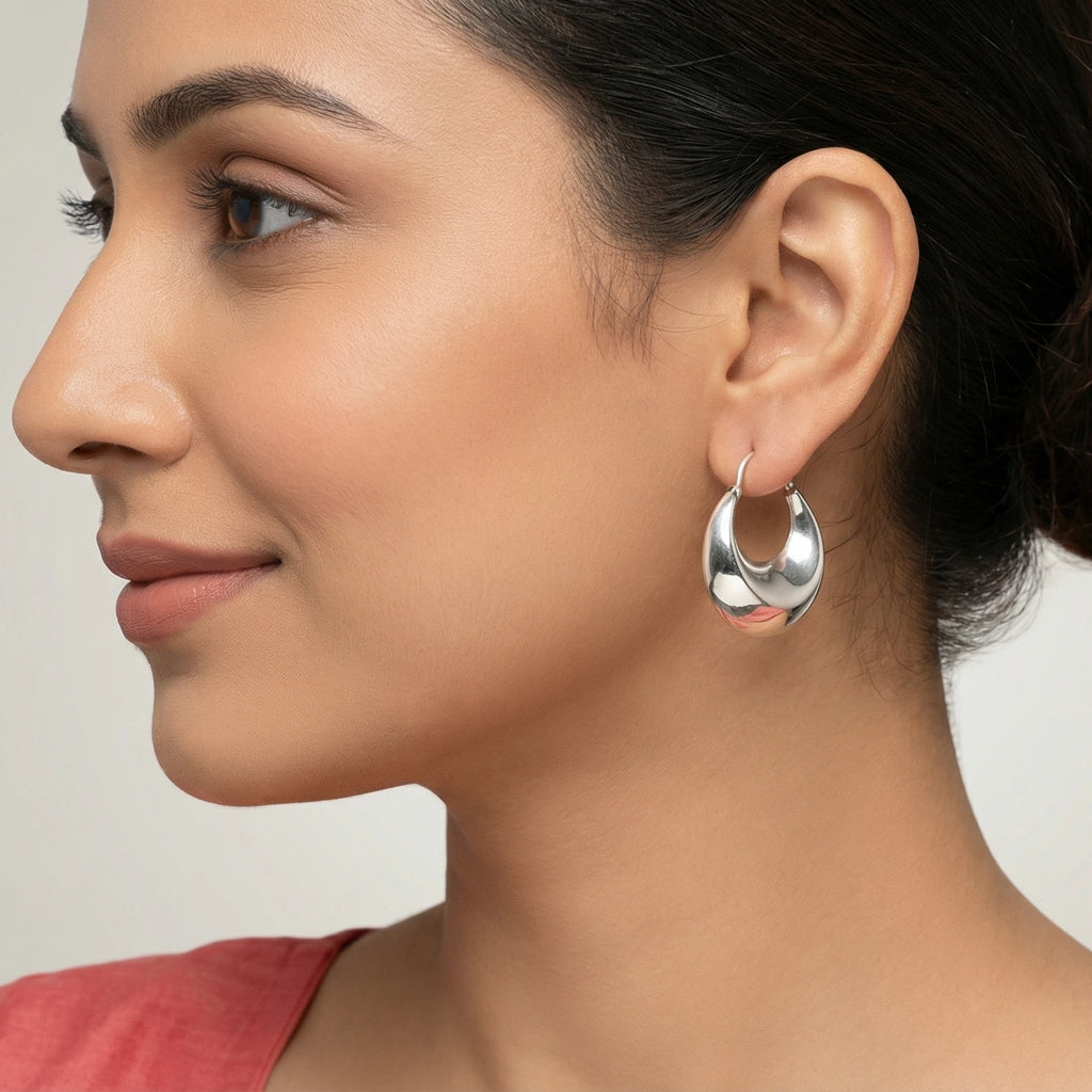 Close-up of a woman wearing silver matka hoop earrings with a neutral background