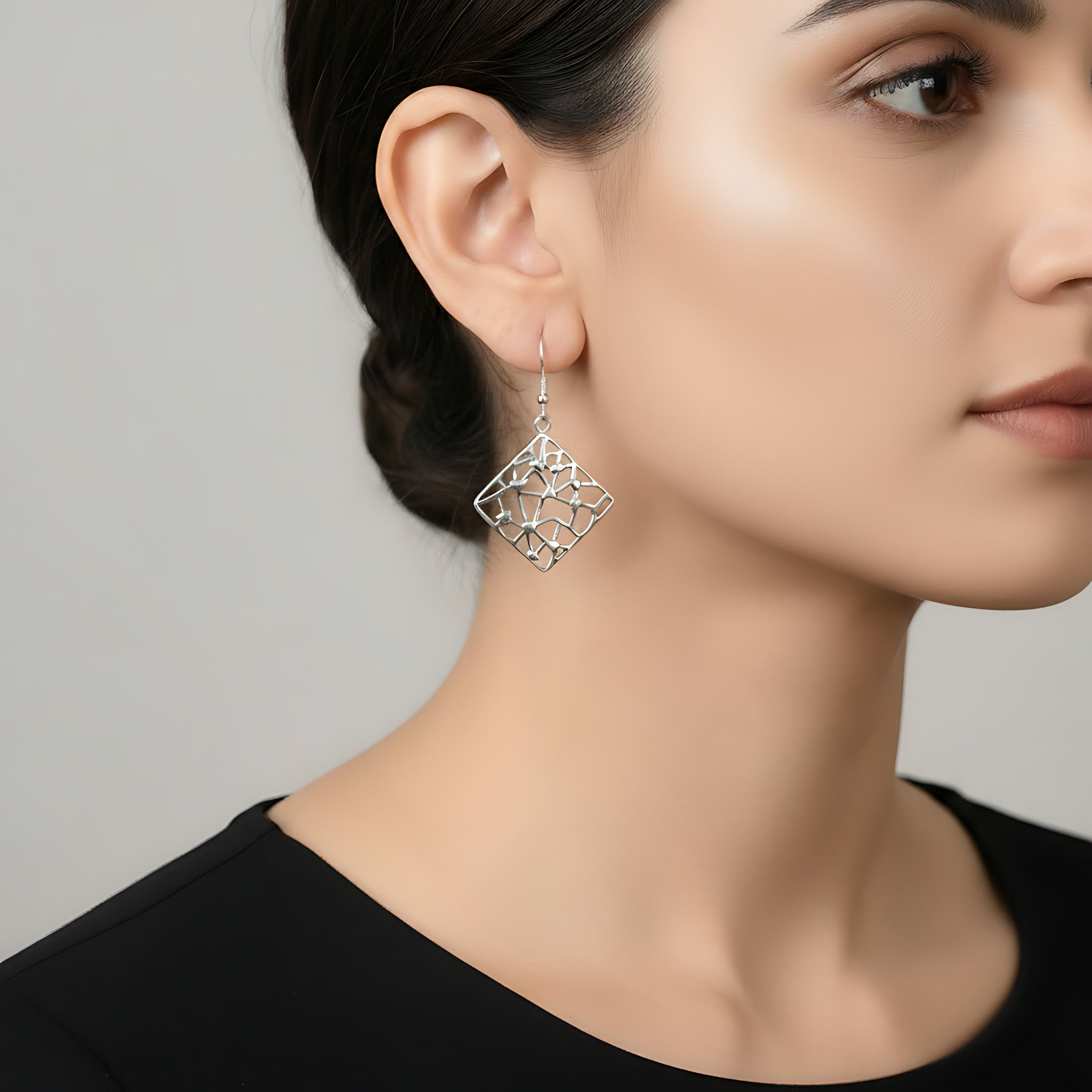 Close-up of a woman wearing a square mosaic silver dangle earring against a neutral background