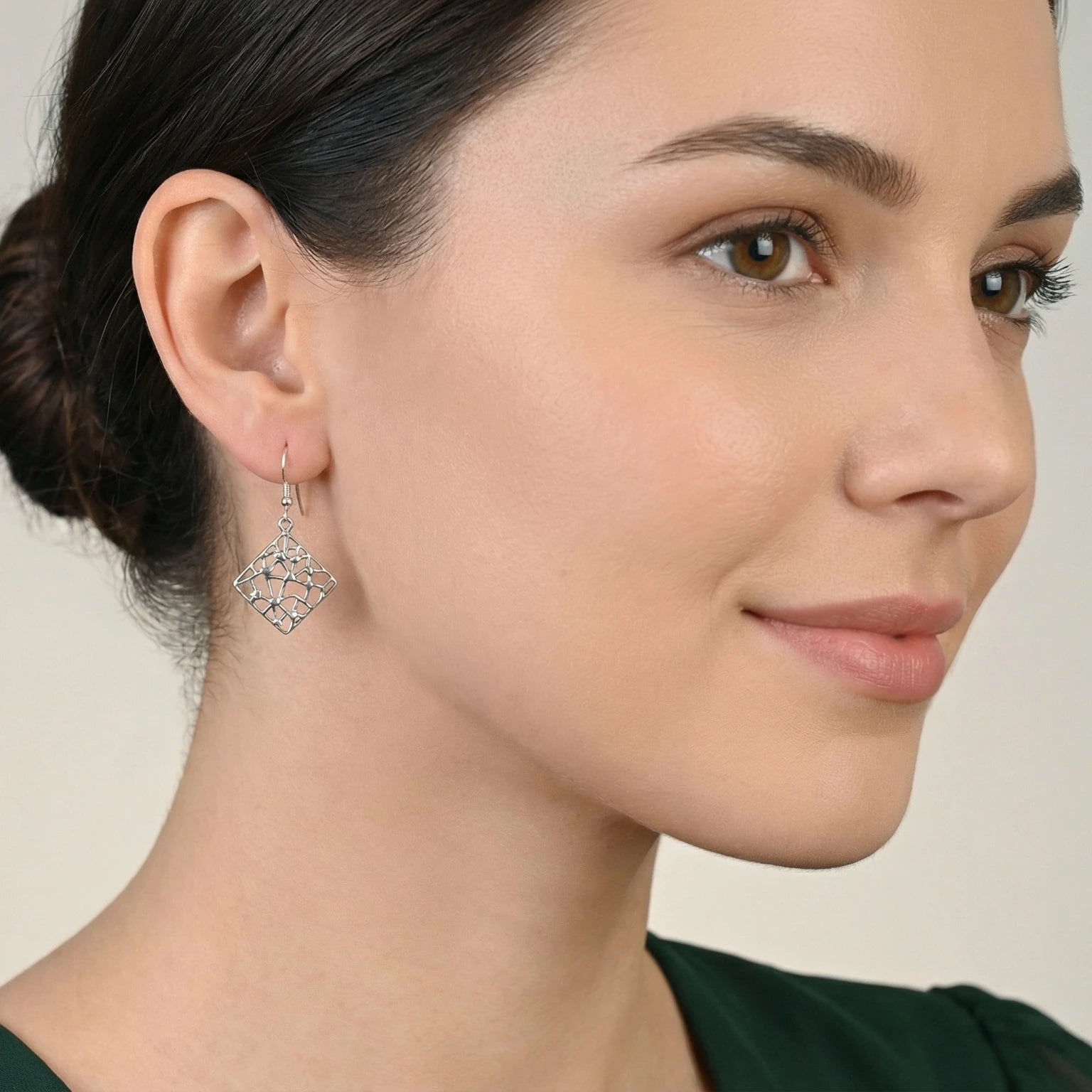 Close-up of a woman wearing a square mosaic silver dangle earring against a neutral background
