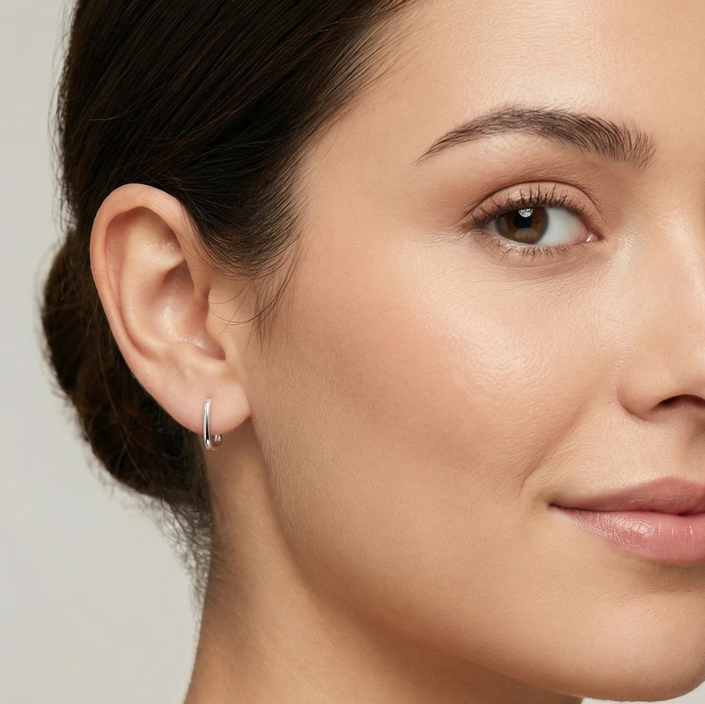 Close-up of an ear wearing a silver rectangular hoop earring with a blurred background