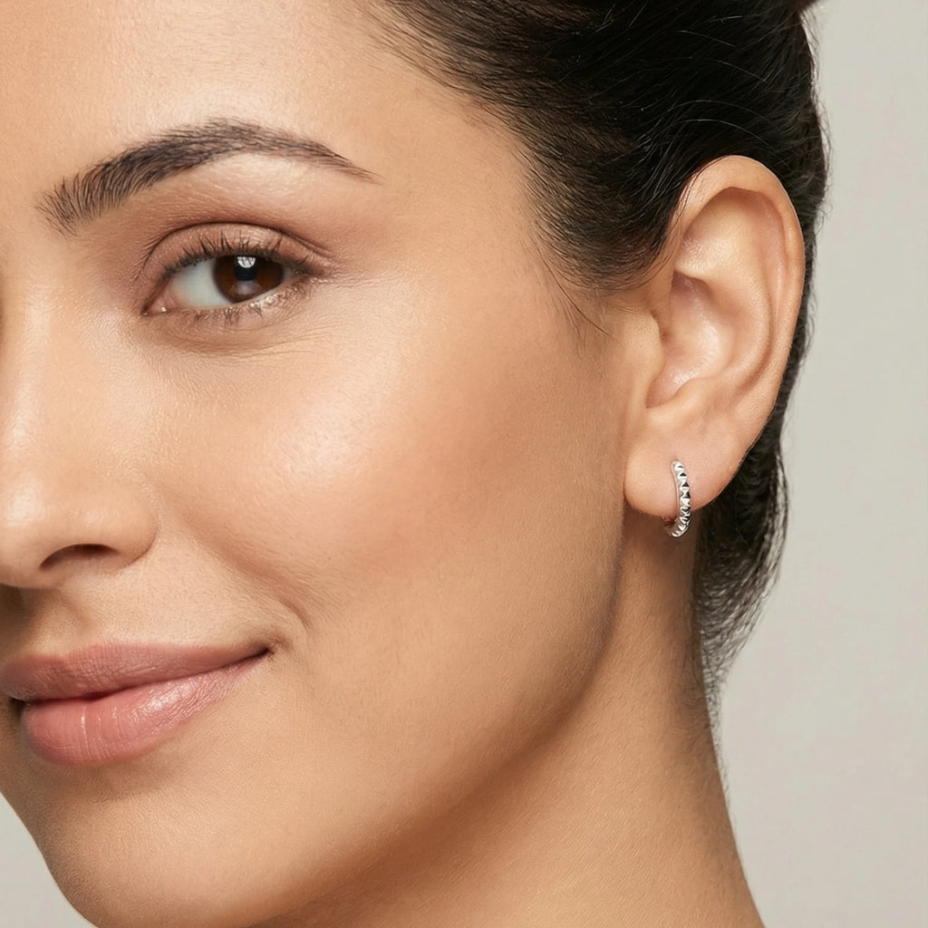 Close-up of an ear wearing a small spiked style silver hoop earring.