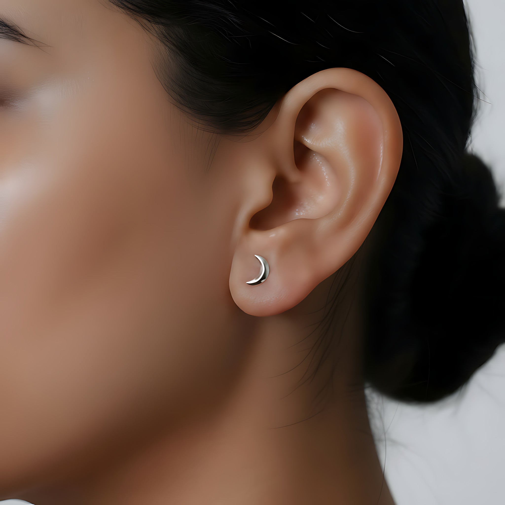 Close-up of an ear wearing a crescent moon stud earring with a blurred background