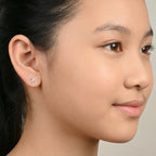 Close-up of a young girl with styled hair and silver butterfly stud earrings against a neutral background