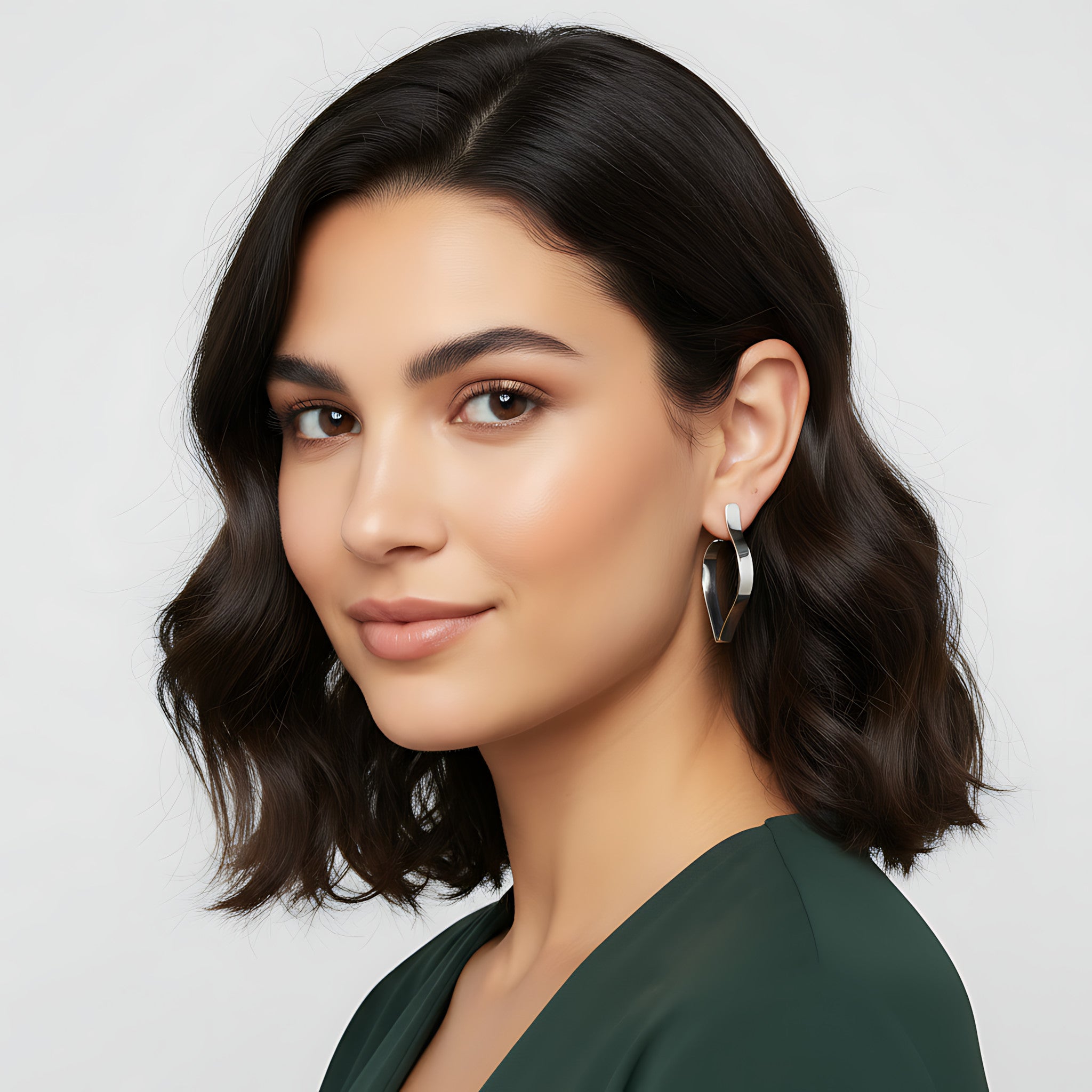 Woman with styled hair wearing a shiny silver petal-shaped stud earring against a plain background
