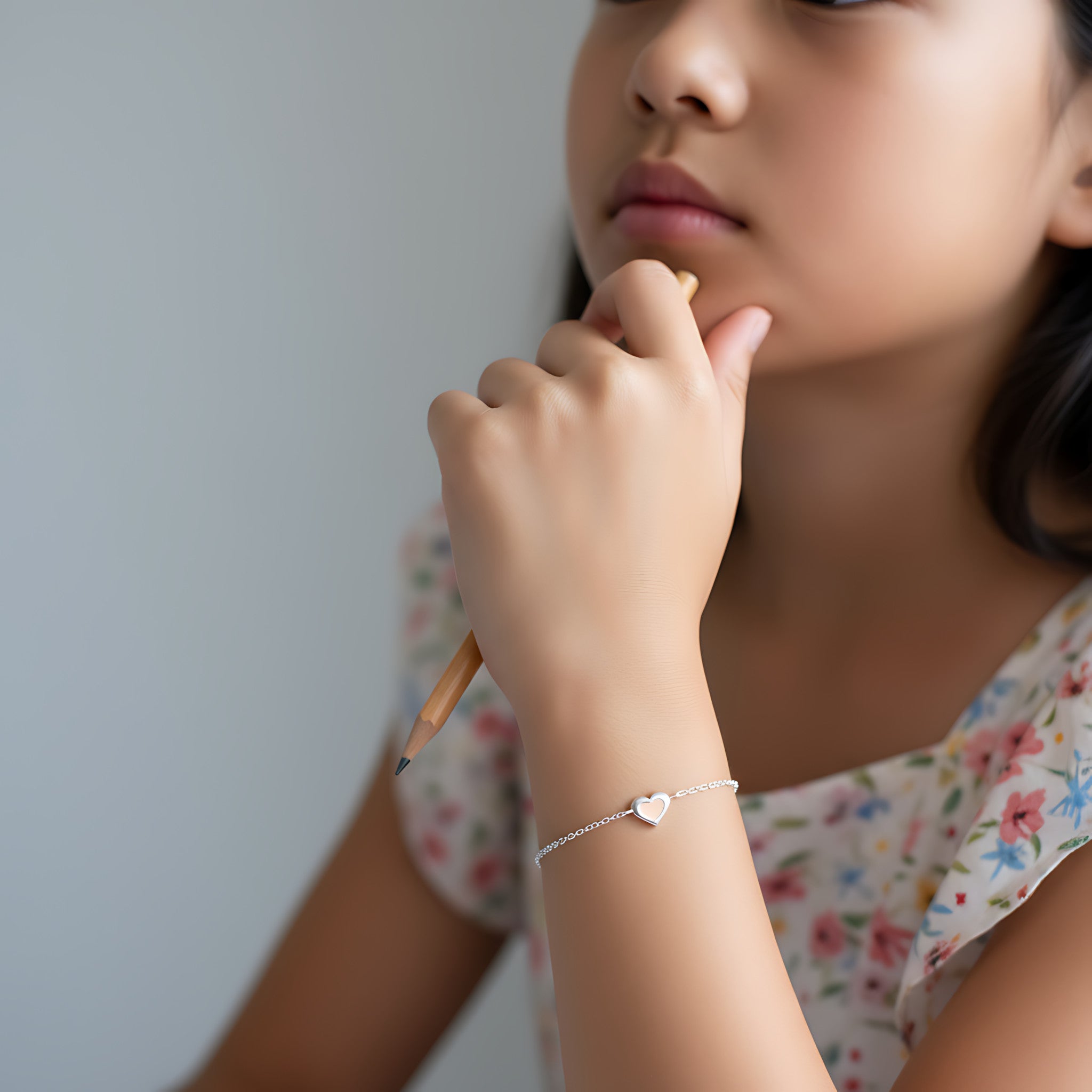 Close-up of a young girl with a pencil in her hand wearing a heart-shaped silver bracelet on a plain background