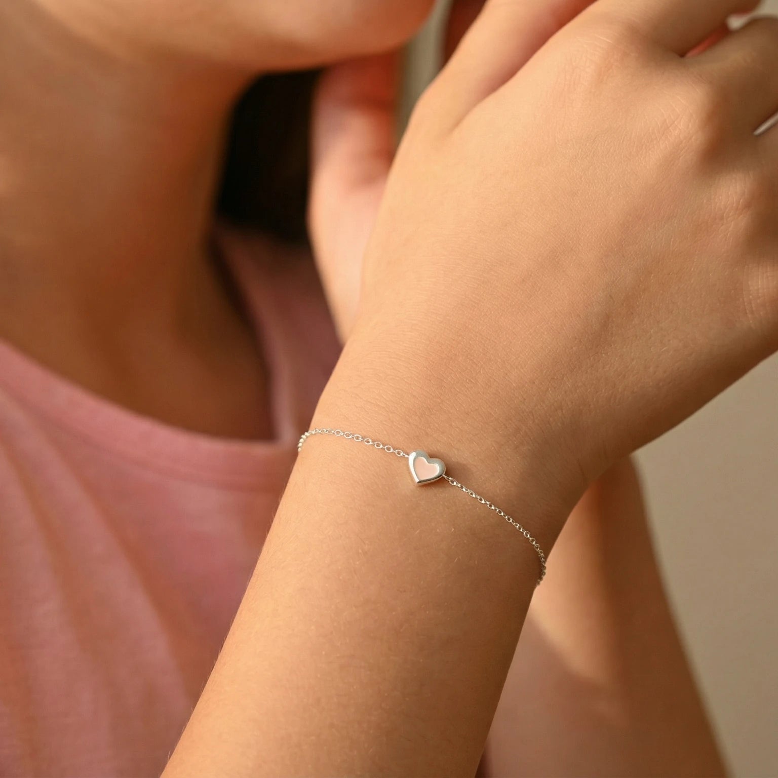Close-up of a young girl's wrist wearing a heart-shaped silver bracelet on a plain background