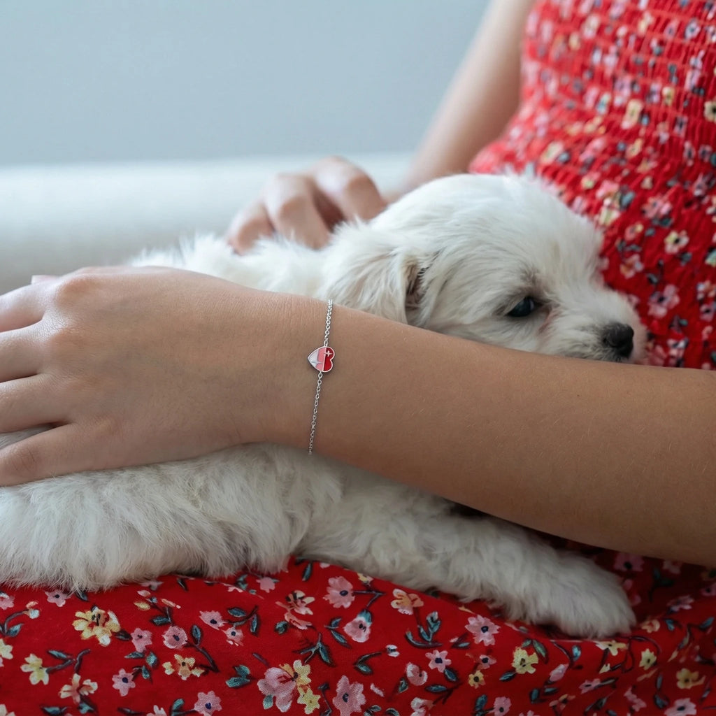 Closeup of a girl's arm wearing a silver heart bracelet and a red floral dress holding a small white dog