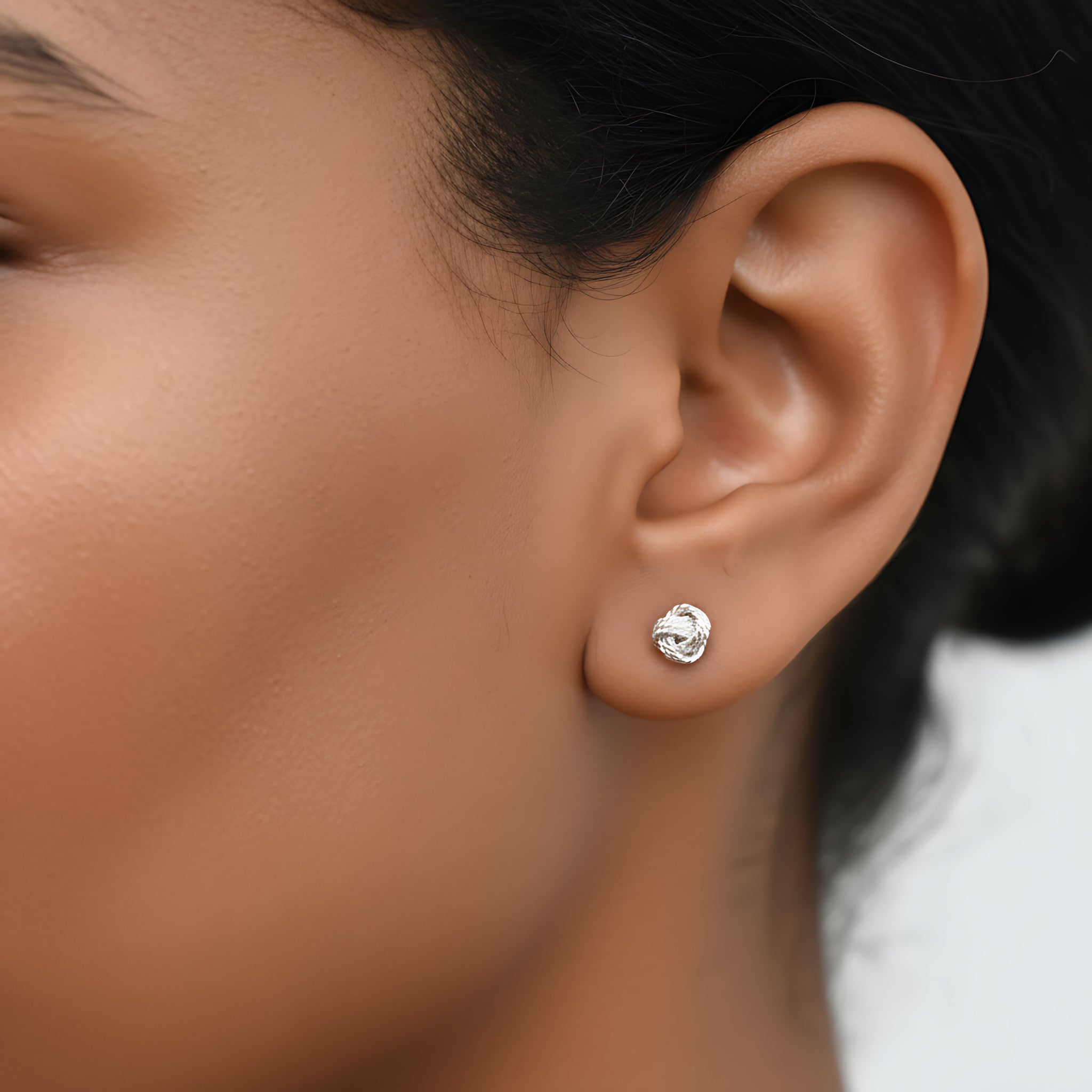 Close-up of an ear wearing a knot shaped silver stud earring with a blurred background