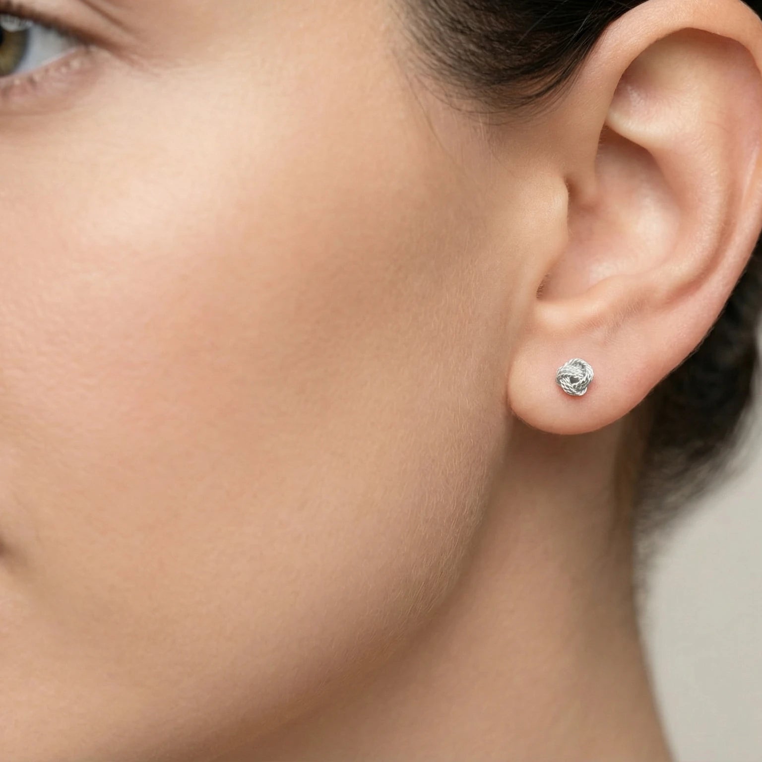 Close-up of an ear wearing a knot shaped silver stud earring with a blurred background