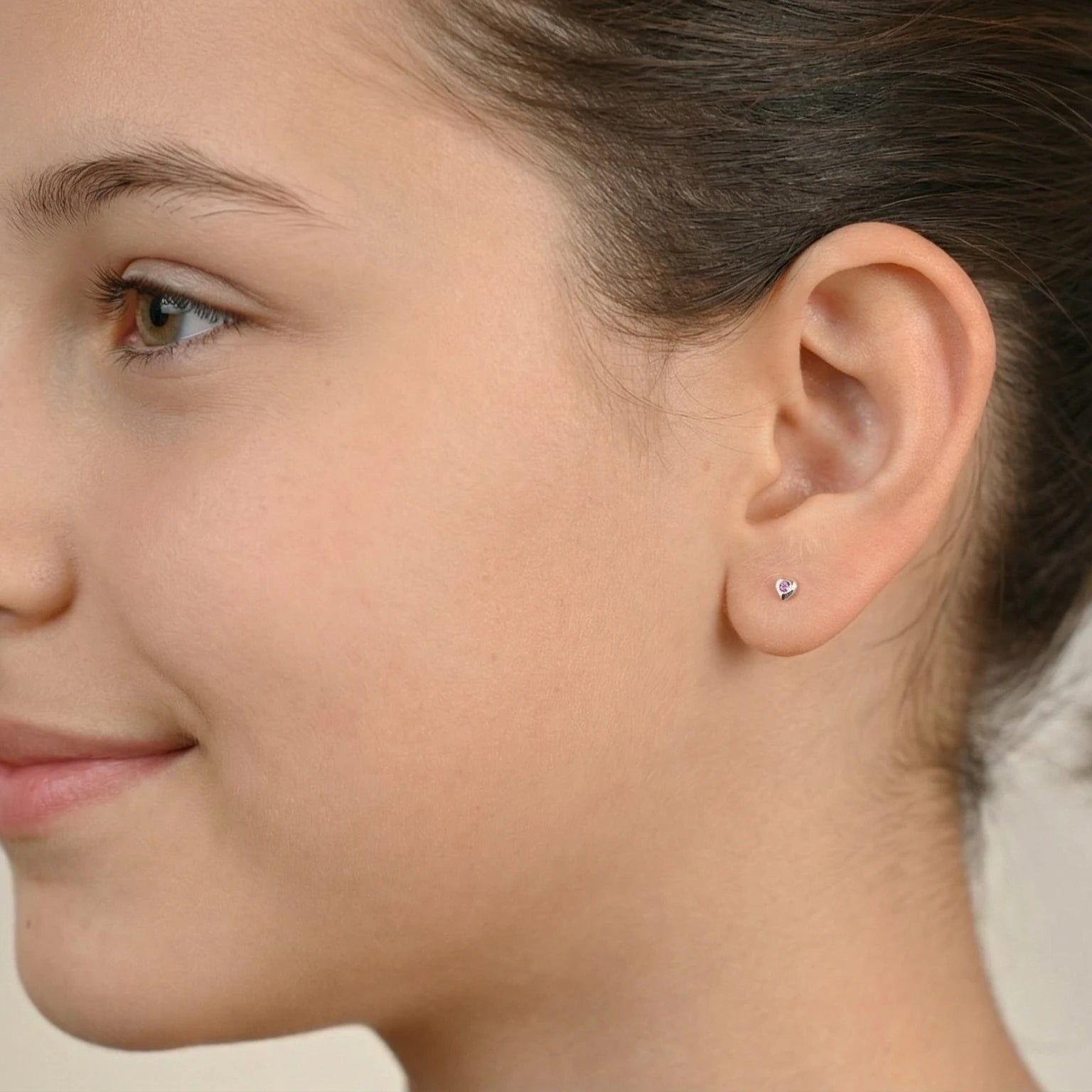 Closeup of a girl wearing a silver heart shape stud earring on a neutral background
