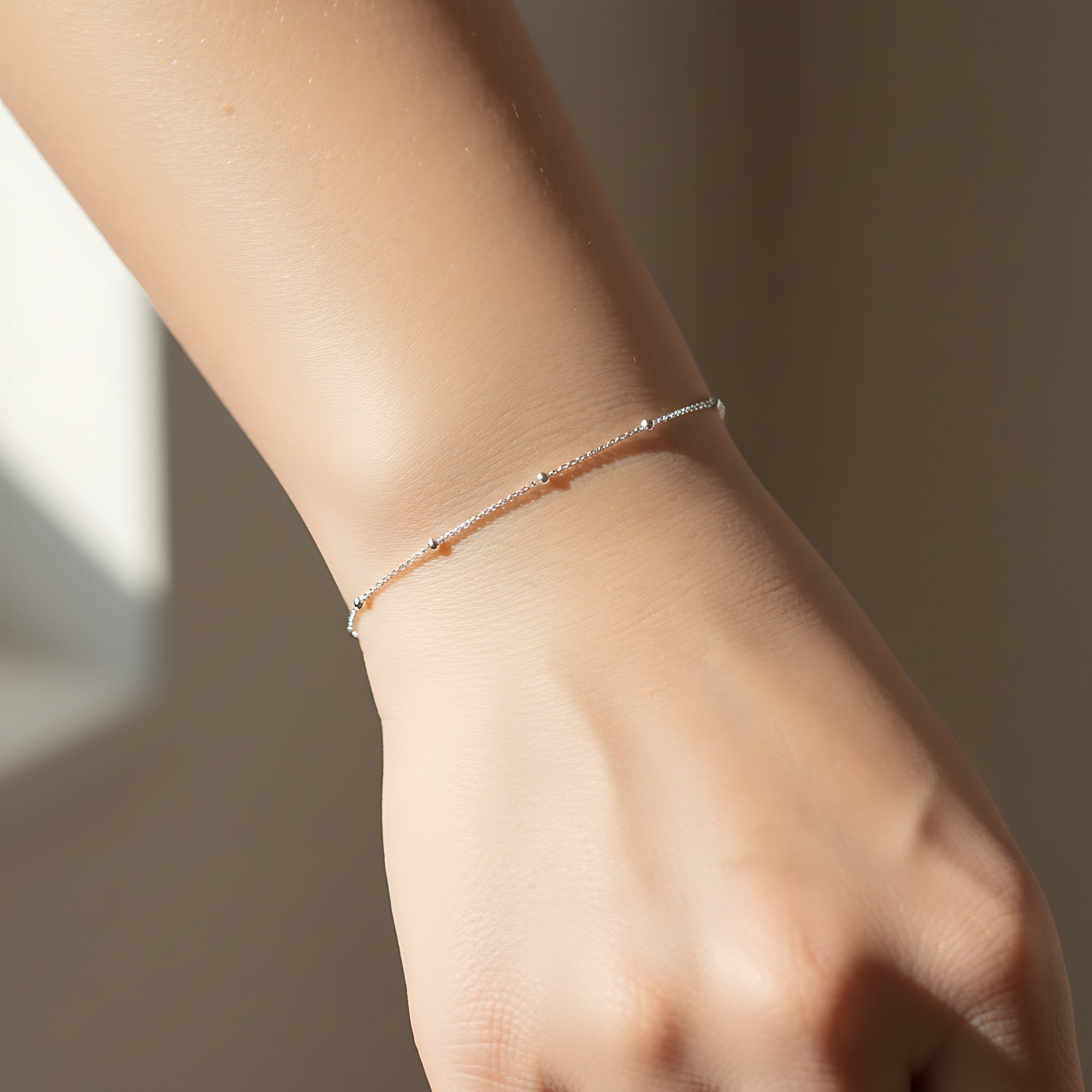 Closeup of a female wrist wearing a silver satellite bracelet against a neutral background