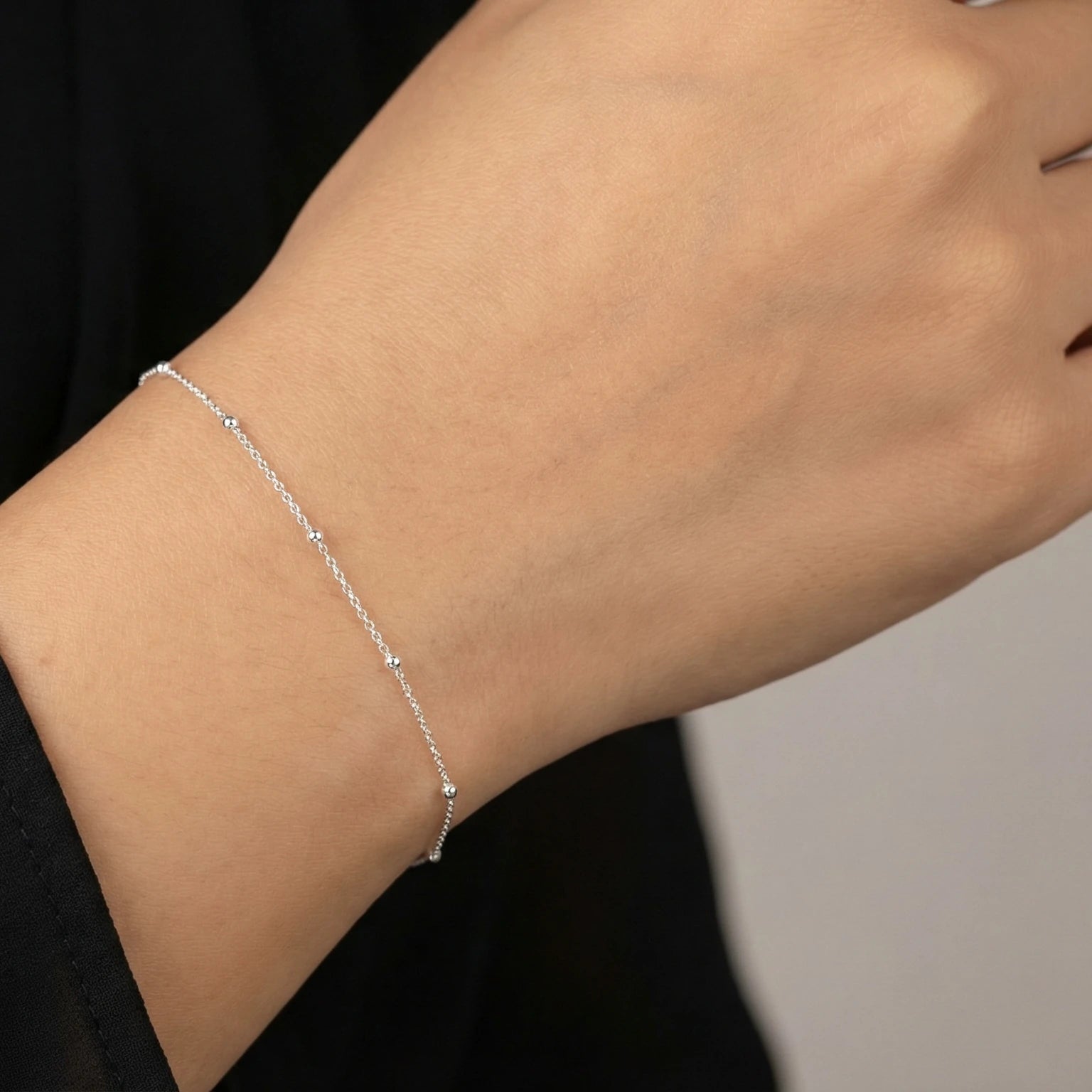Closeup of a female wrist wearing a silver satellite bracelet against a neutral background