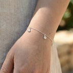 Silver bracelet with shell charms on a wrist against a blurred natural background