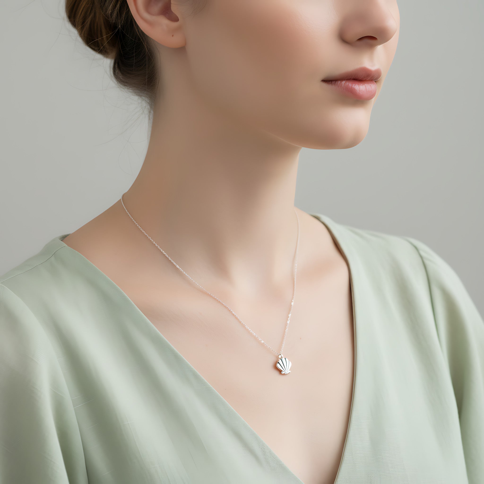 Woman wearing a delicate necklace with a small shell pendant against a neutral background