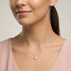 Woman wearing a delicate necklace with a small shell pendant against a neutral background