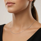 Close-up of a person wearing a delicate silver Singapore chain against a neutral background