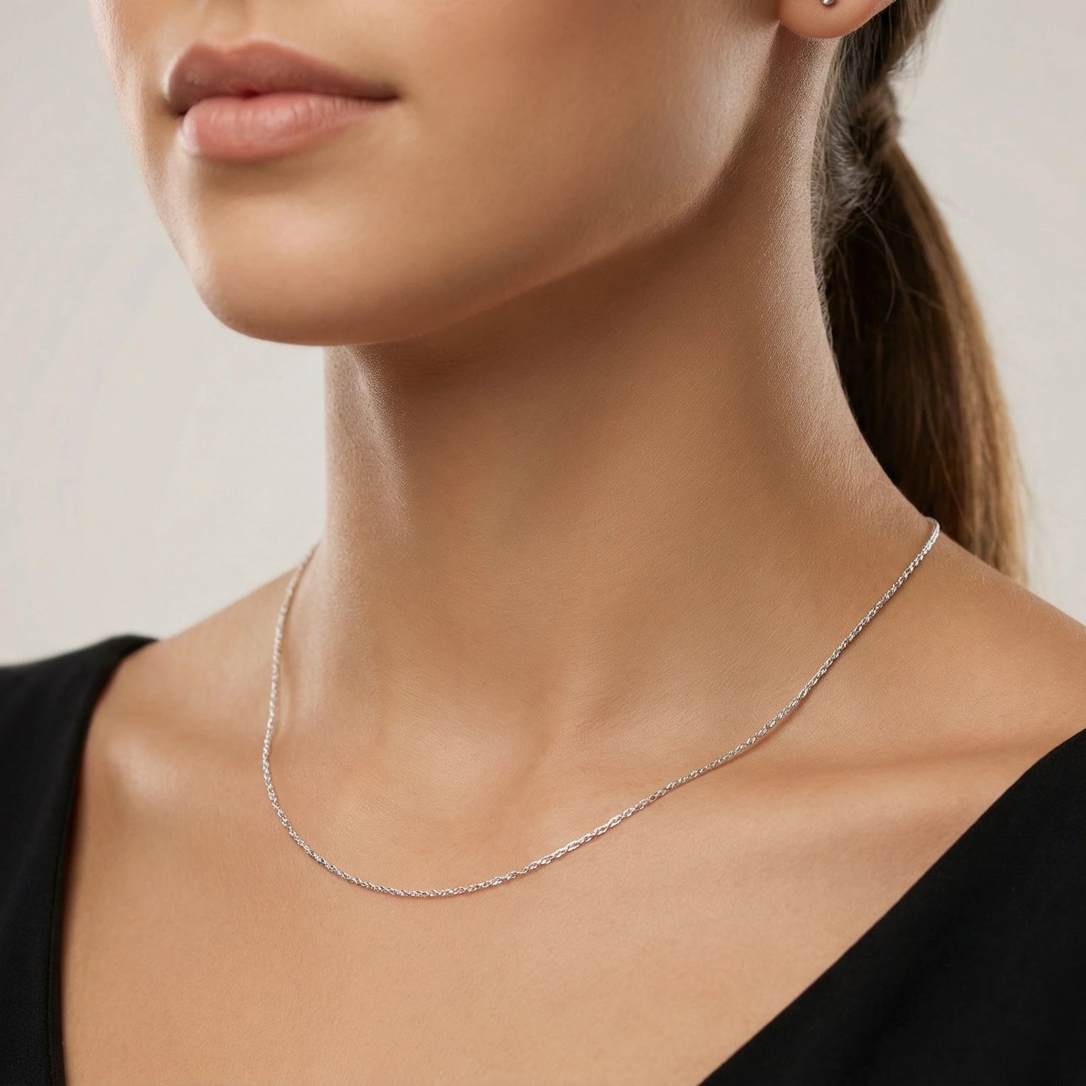 Close-up of a person wearing a delicate silver Singapore chain against a neutral background